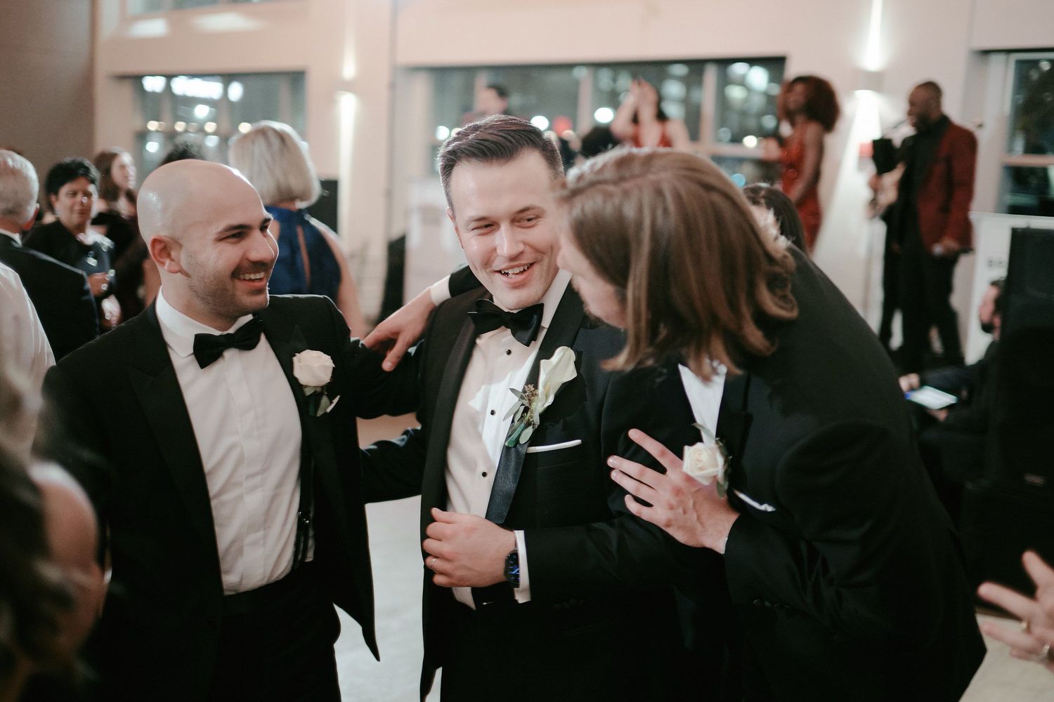 A group conversing and laughing together at a formal black tie event in an indoor venue.