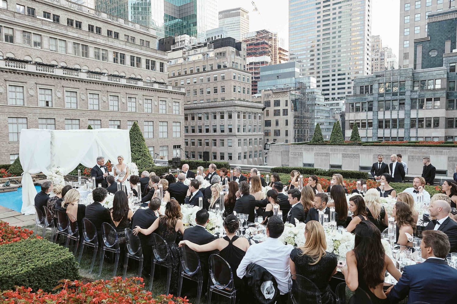 Elegant rooftop wedding reception at a New York City venue with guests seated at long tables surrounded by skyscrapers.