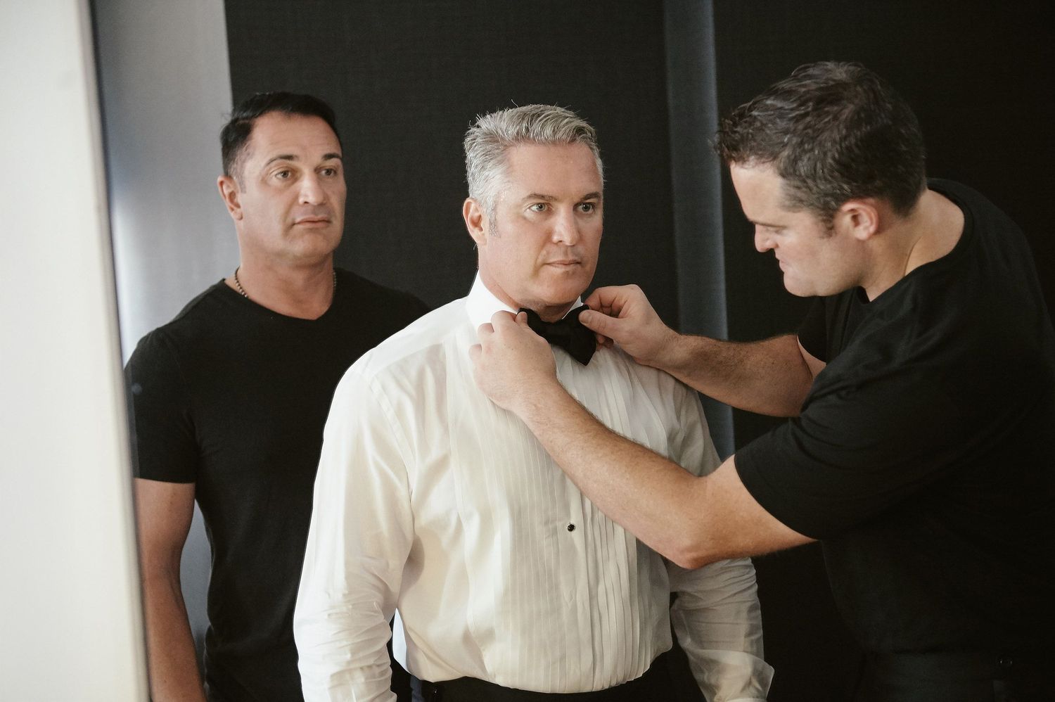 A person in a white dress shirt gets their collar adjusted while another stands by in black attire.