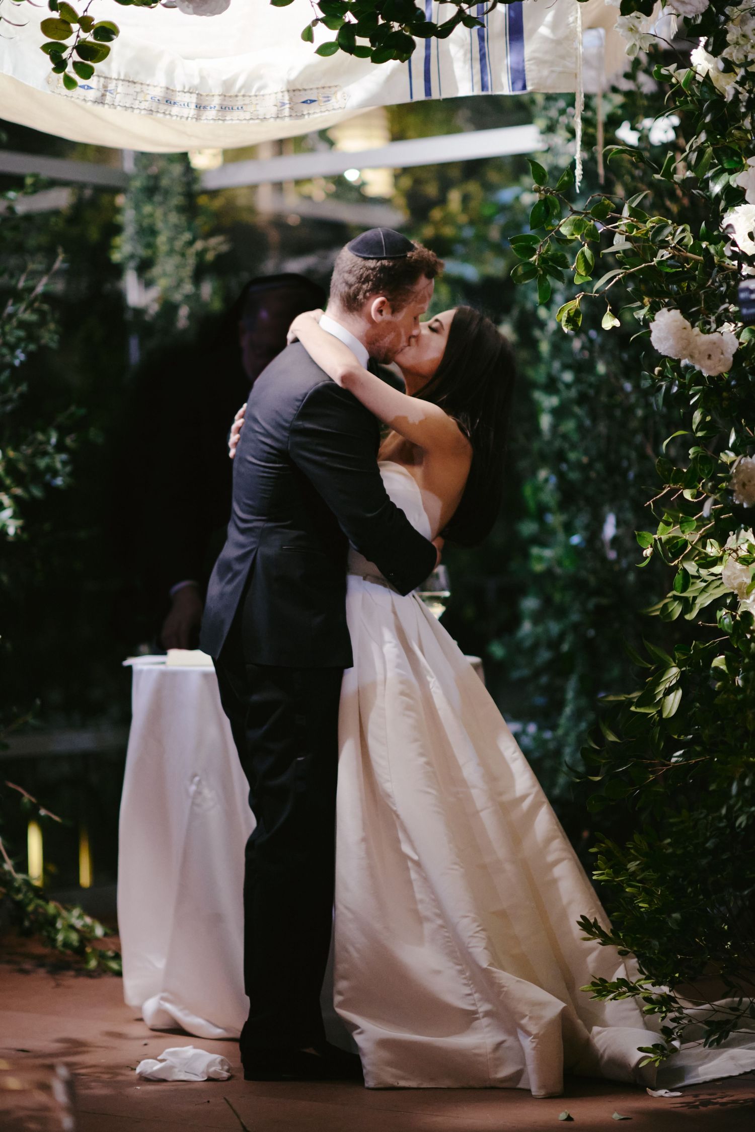 A romantic wedding moment surrounded by white flowers and greenery in an intimate outdoor garden setting.
