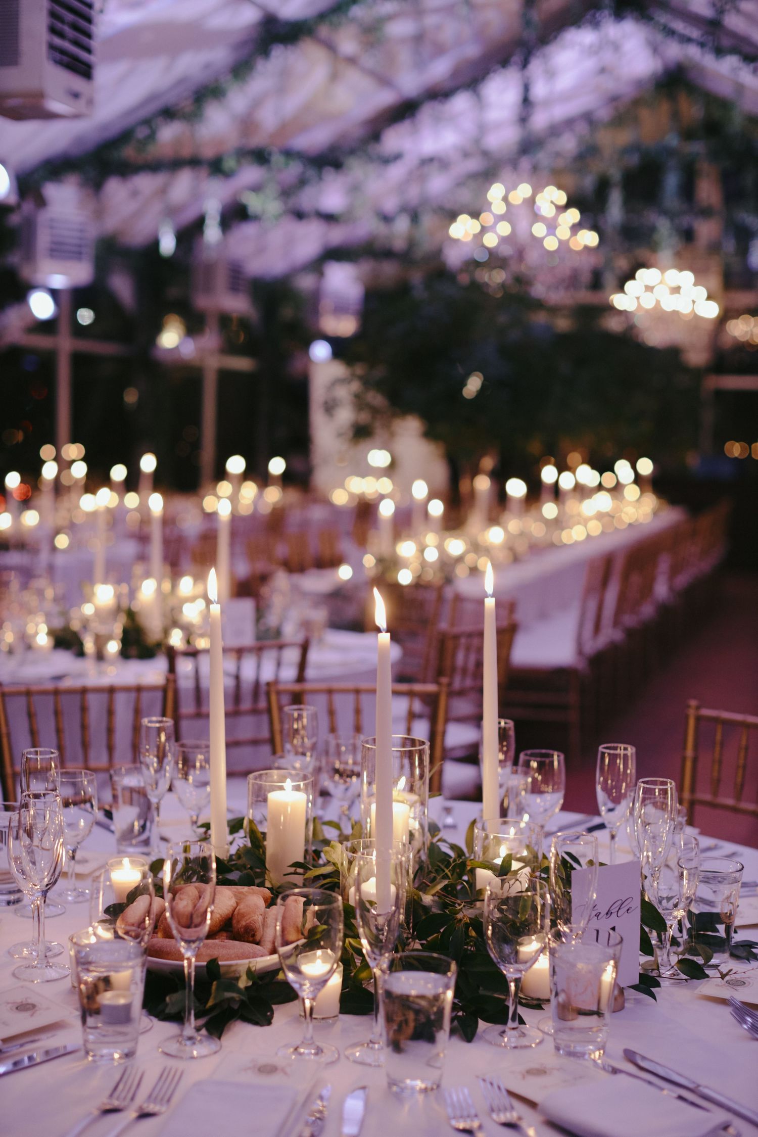 Elegant wedding reception table with white taper candles, floral centerpieces, and crystal glassware under twinkling lights.