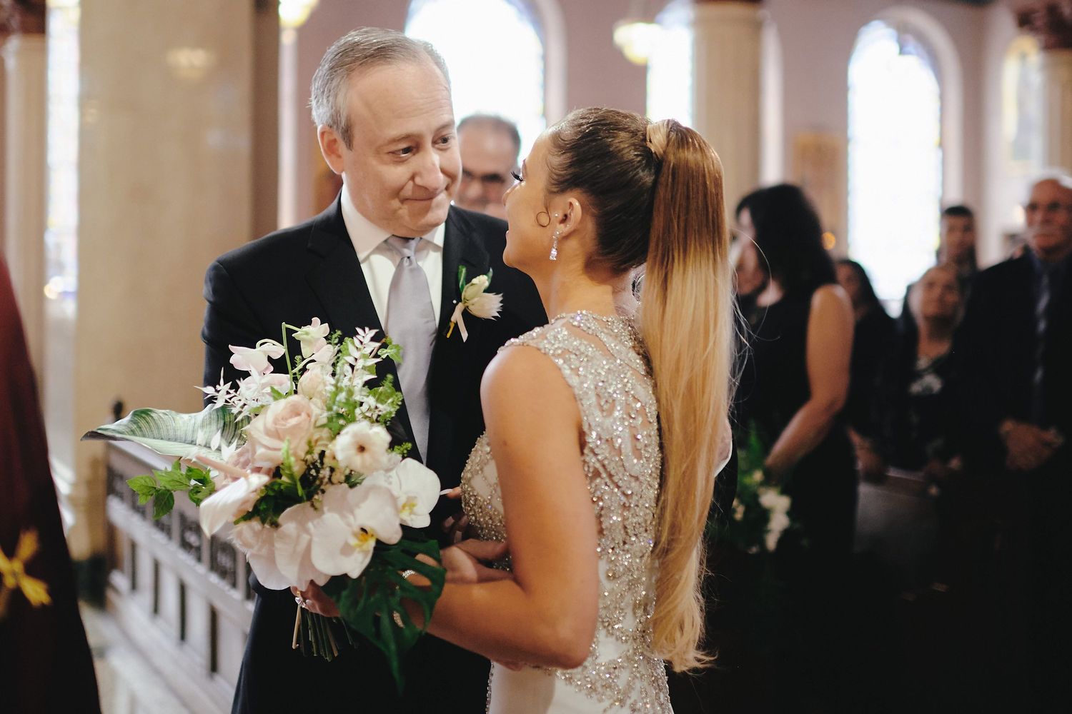 Couple shares an intimate moment during church wedding ceremony with bride holding pastel floral bouquet.
