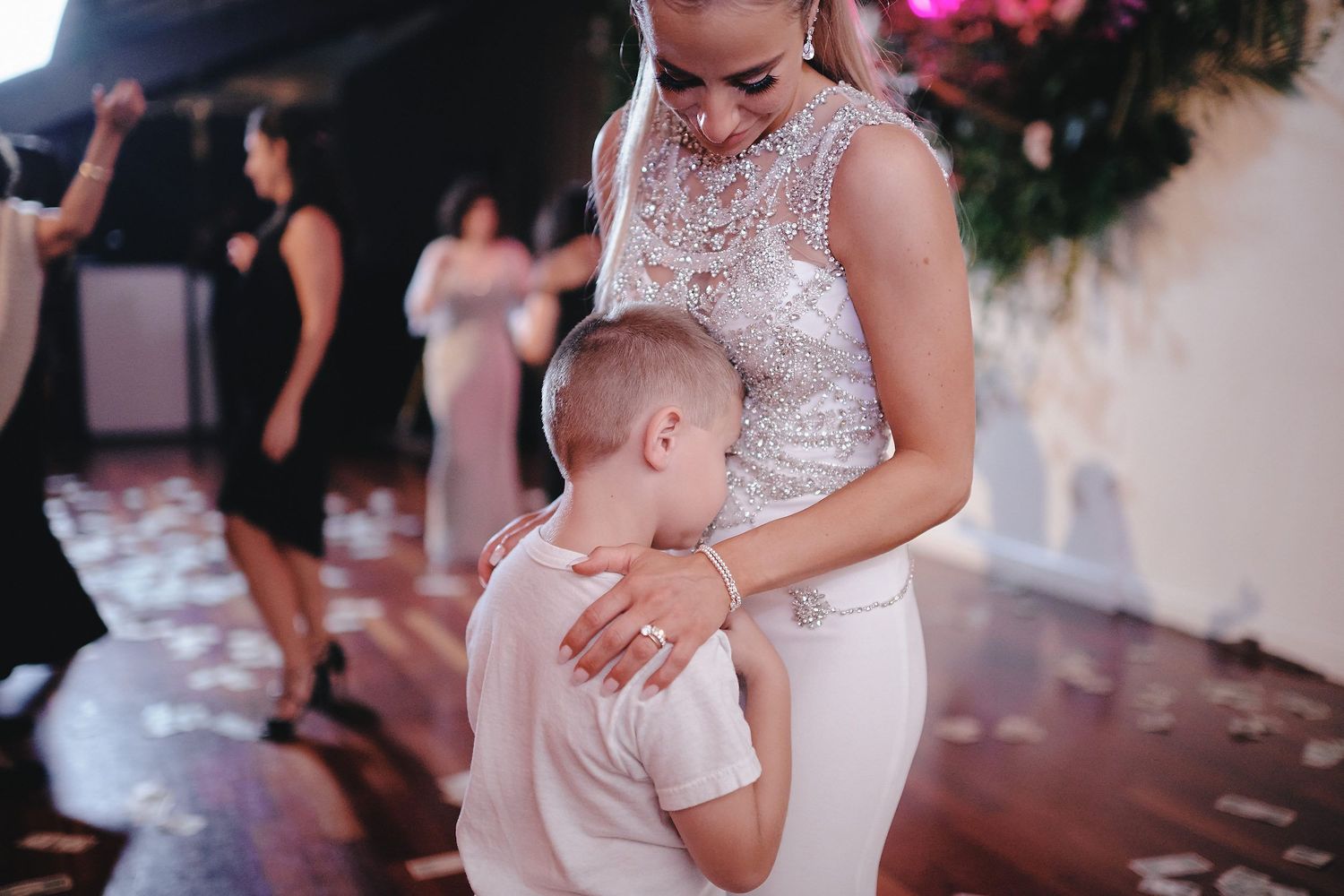 A child in white hugs a woman wearing a lace dress at what appears to be a wedding reception.