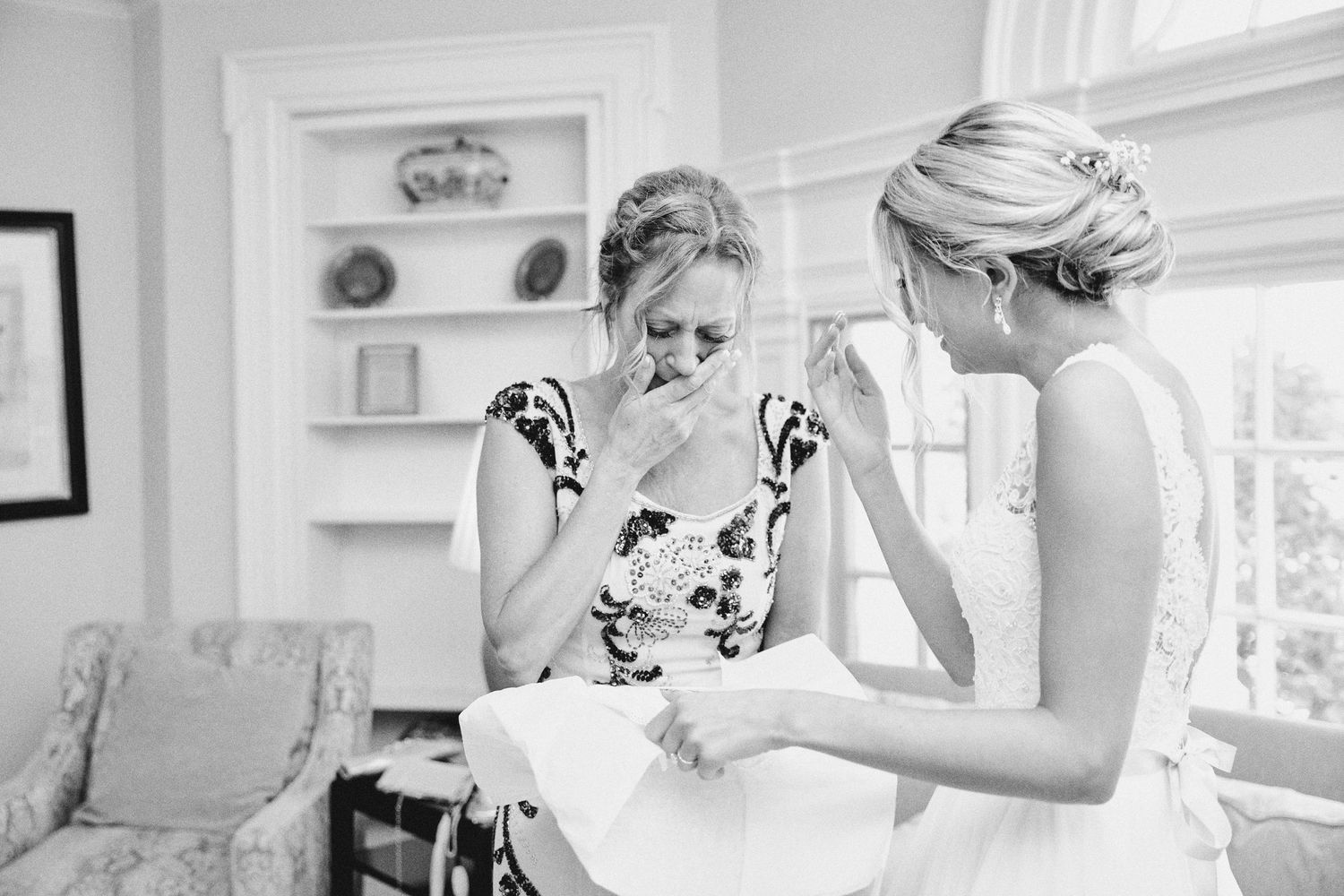 Black and white photo of bride sharing emotional moment with bridesmaid during wedding preparations indoors.