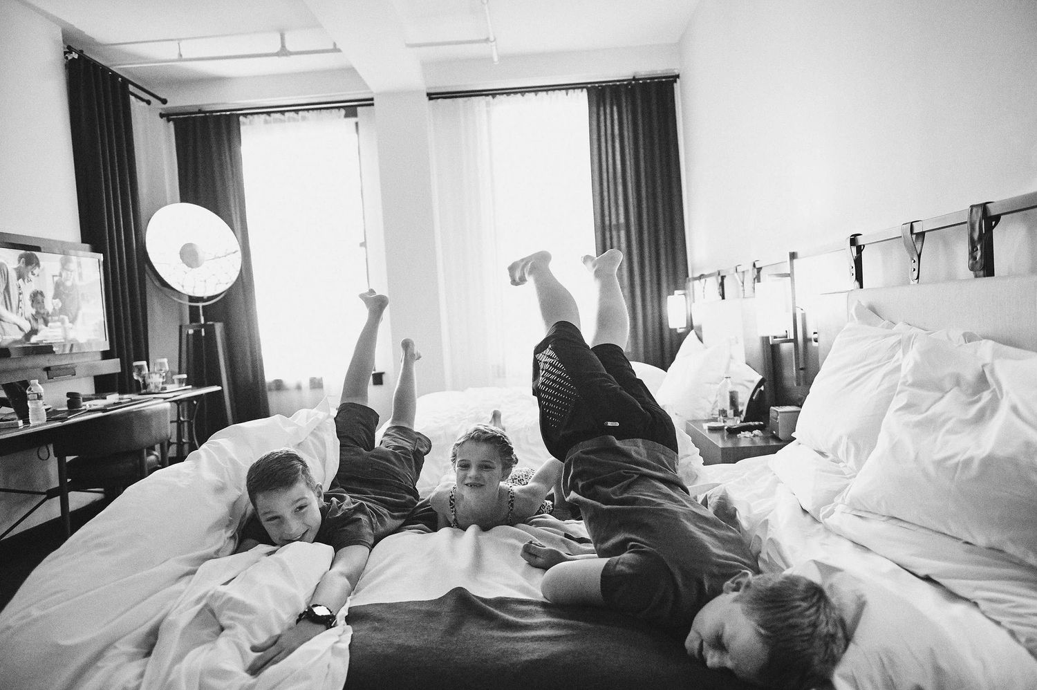 Black and white photo showing people relaxing together on a bed in a casual setting.