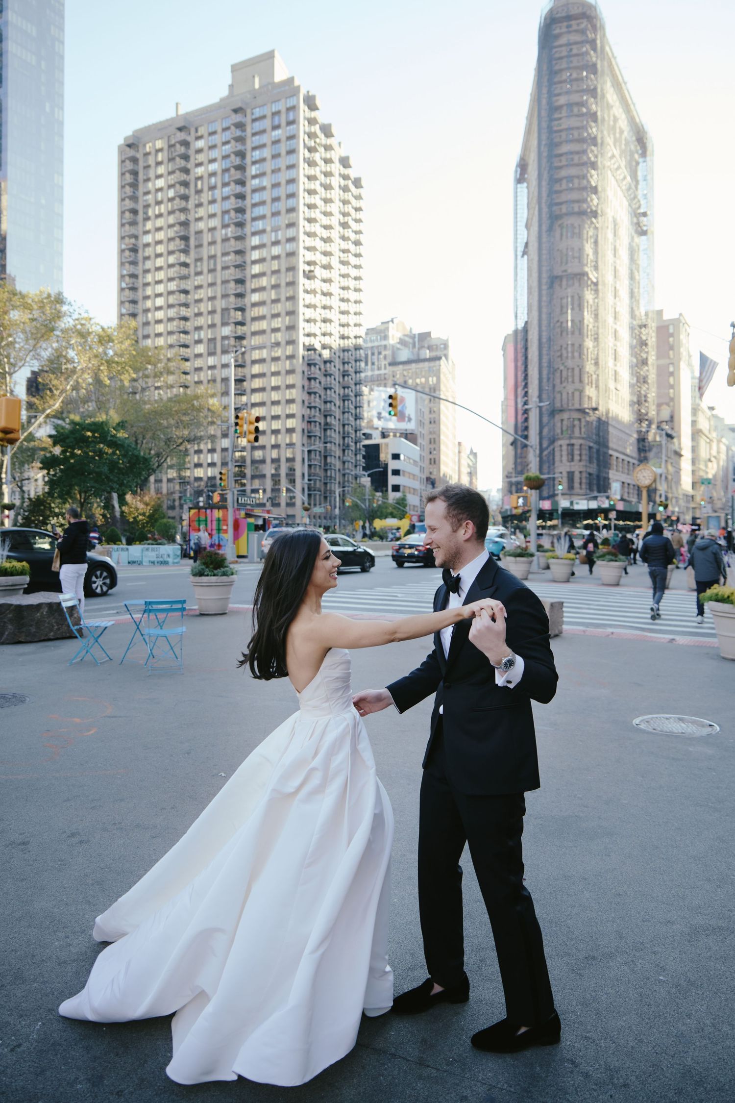 A couple in wedding attire dancing on the street near the historic Flatiron Building in New York City.