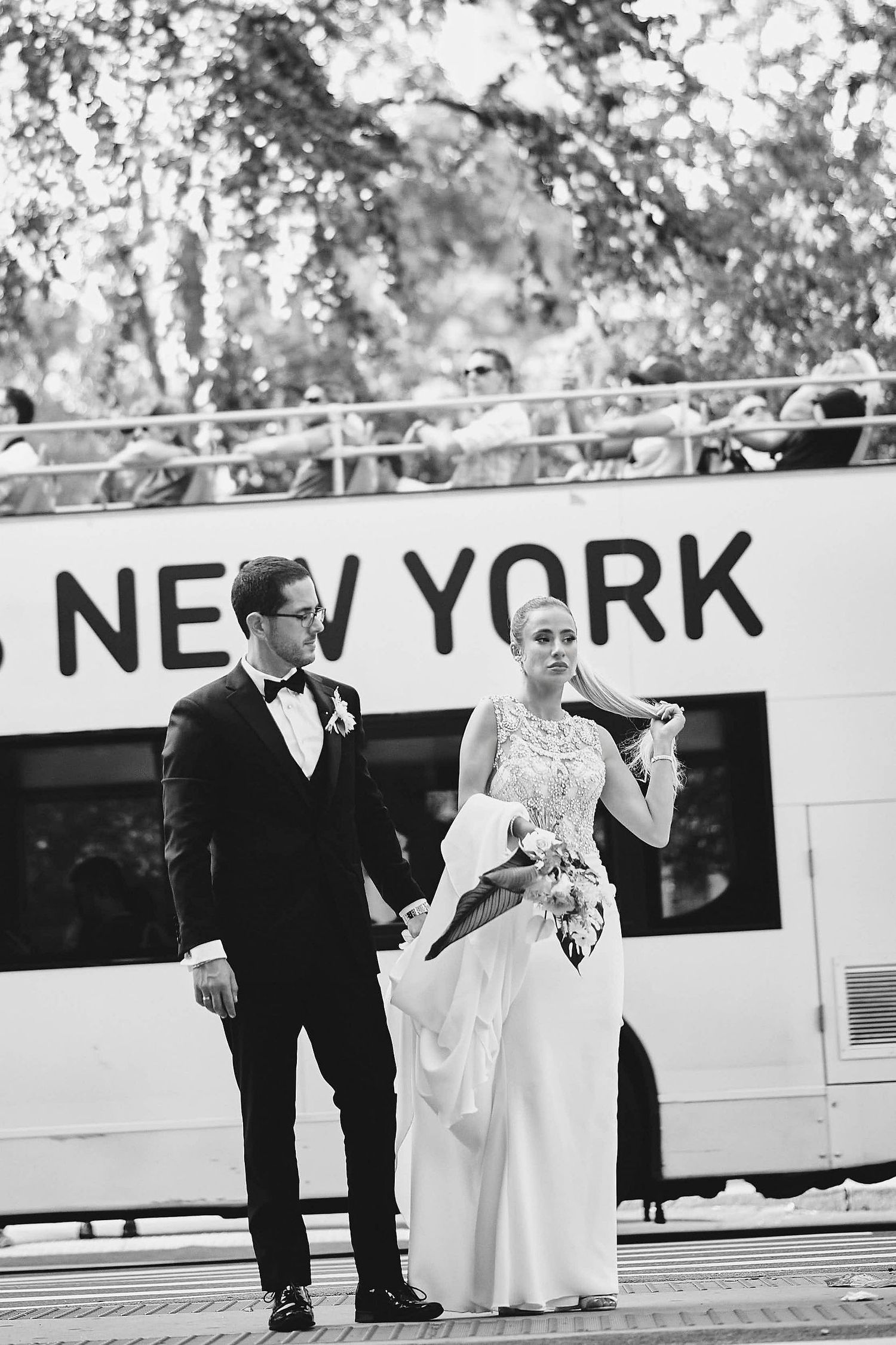 A bride and groom stand together in formal wedding attire in front of a boat with NEW YORK text visible.