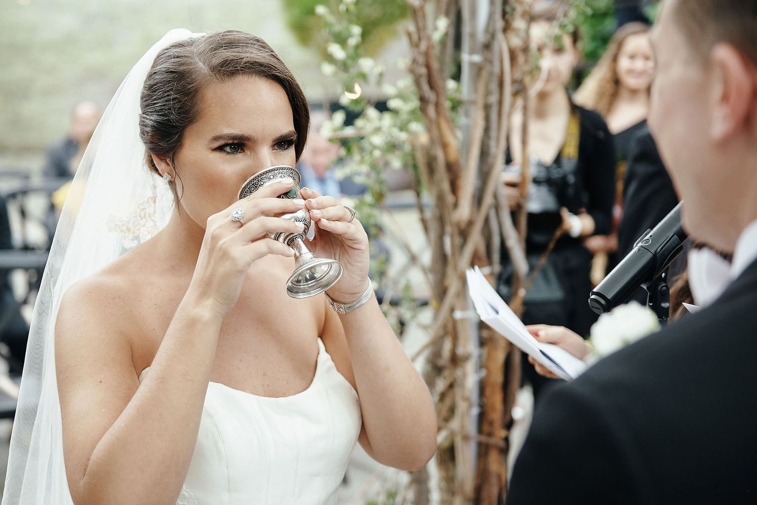 A bride takes a sip from her champagne glass during an outdoor wedding celebration.