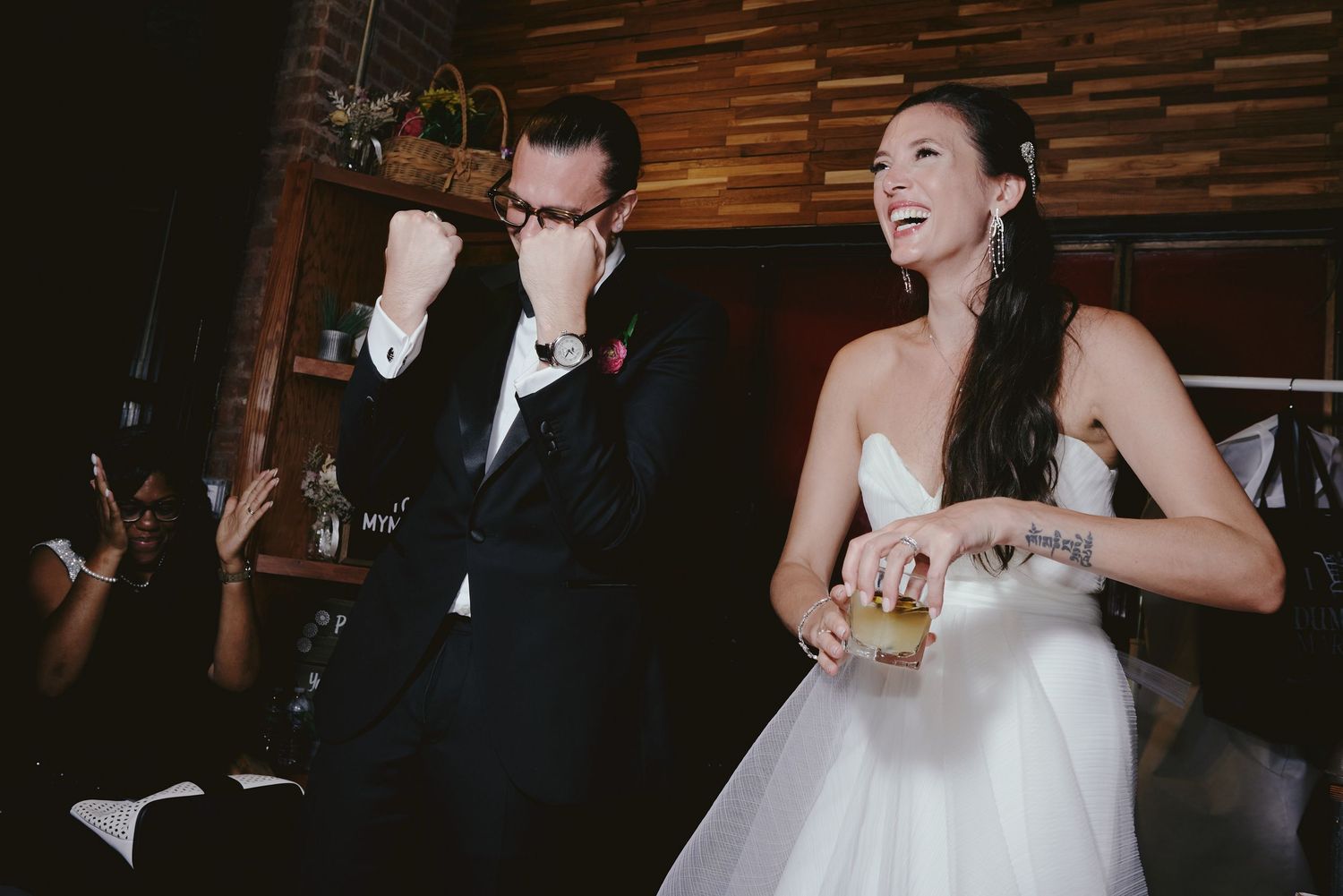 Happy newlyweds share a laugh together while holding their drinks at their indoor wedding reception.