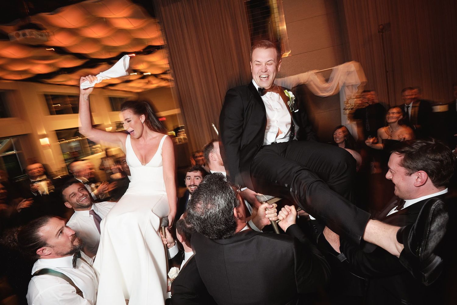 Wedding celebration captured in motion as guests lift and celebrate during a lively reception dance party.