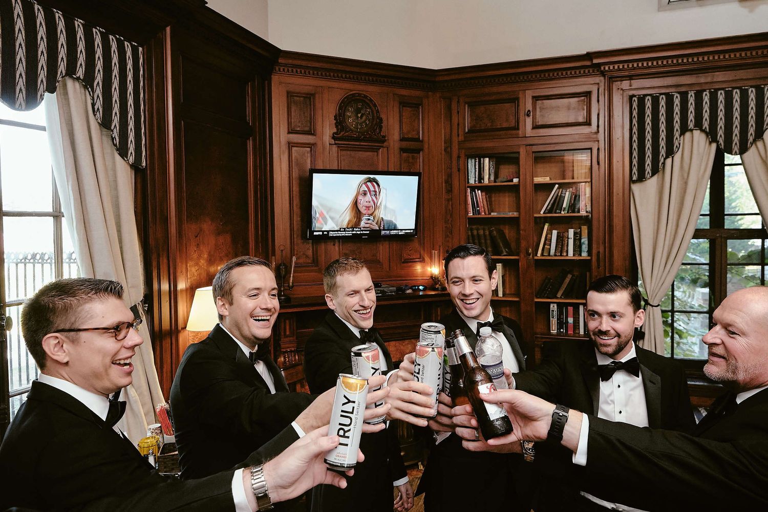 Group toasting with beverages in wood-paneled room with built-in bookshelves and formal attire.