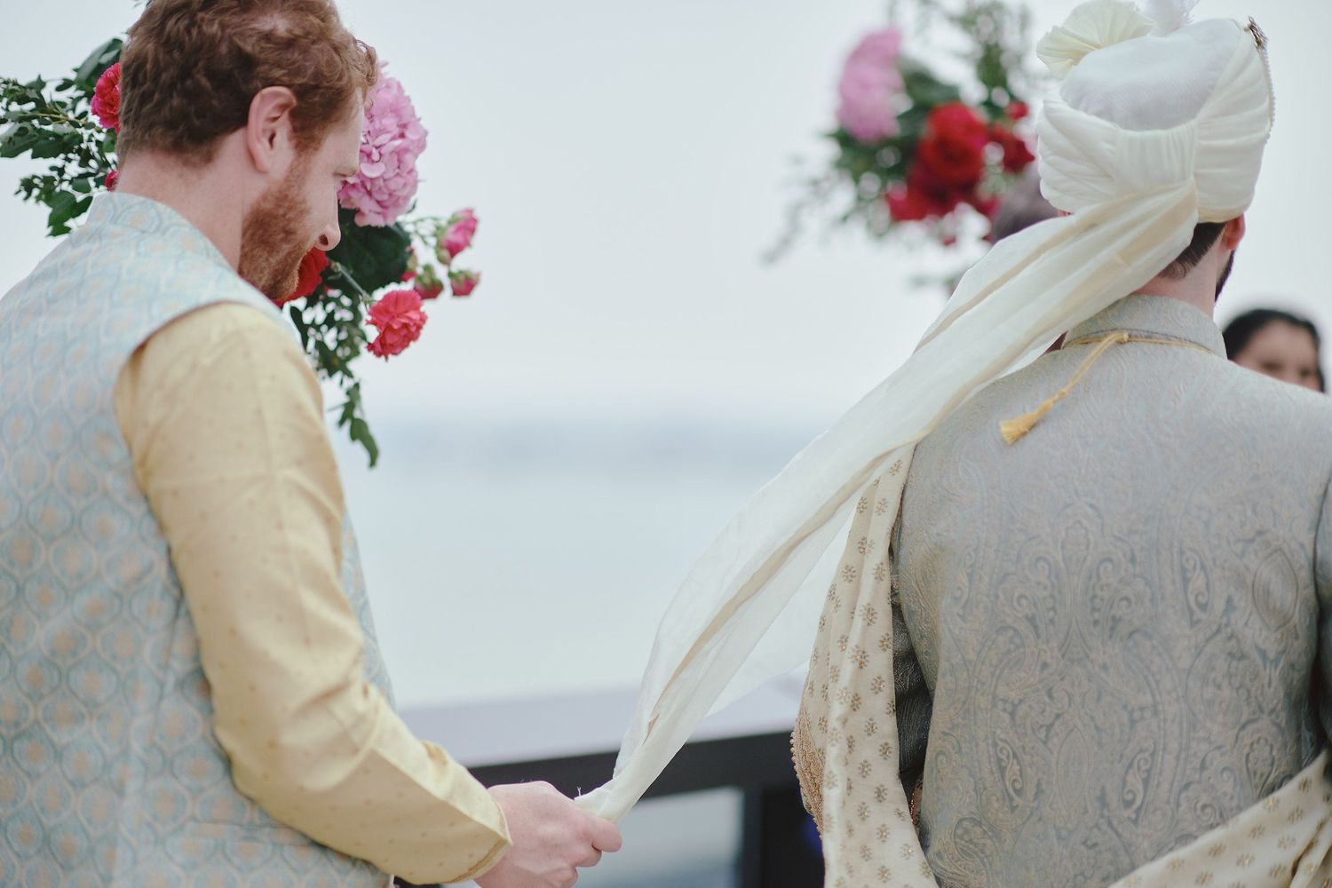 A wedding ceremony with traditional attire and pink floral decorations in the background.