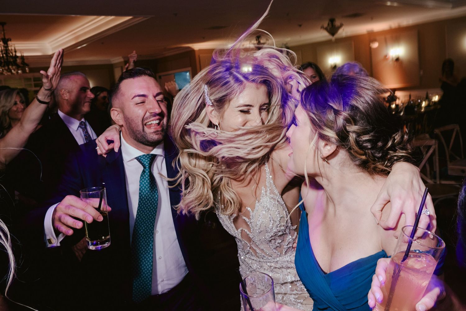 Party guests dancing energetically with colorful hair on a lively dance floor at indoor celebration event.
