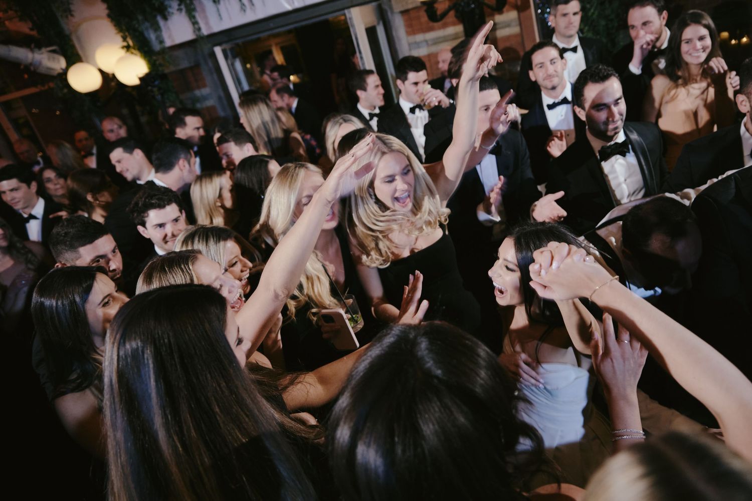 Party guests in formal attire dance and celebrate together on a crowded dance floor at an elegant evening event.