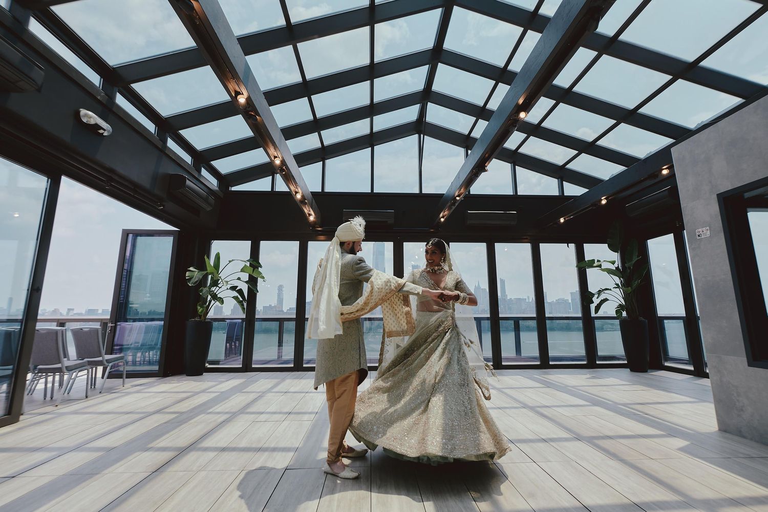 Couple dancing in modern glass-ceiling venue with city skyline visible.