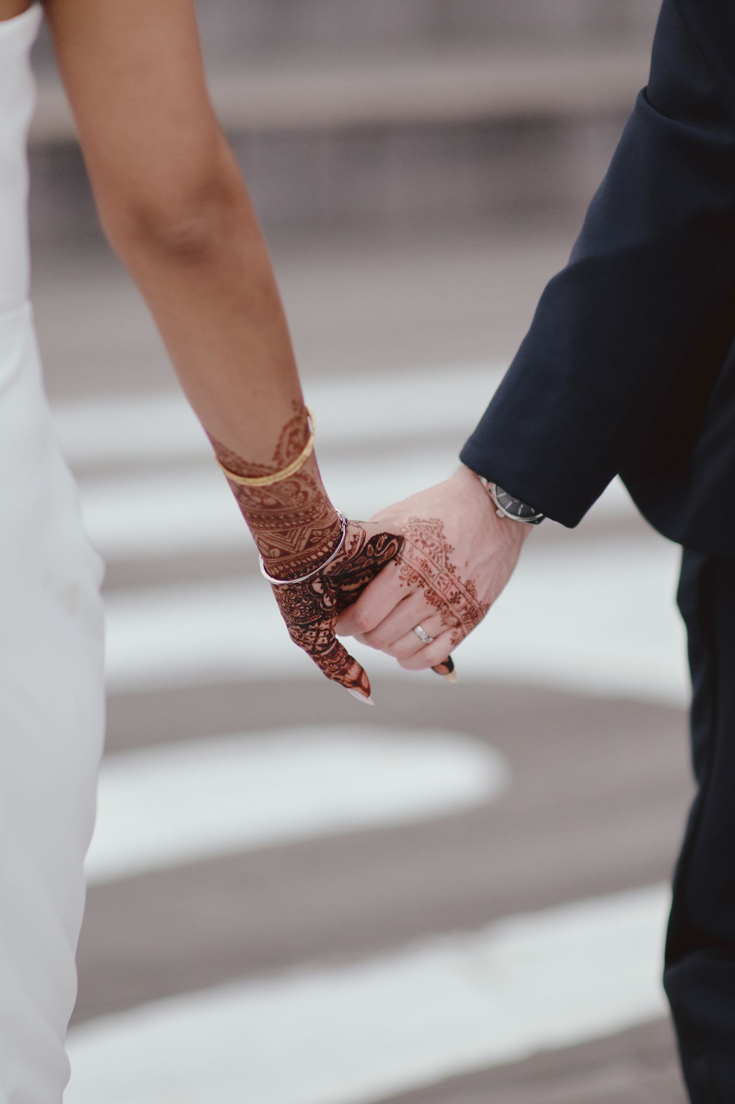 Couple holding hands with intricate henna design adorning one hand, symbolizing a traditional cultural wedding ceremony.
