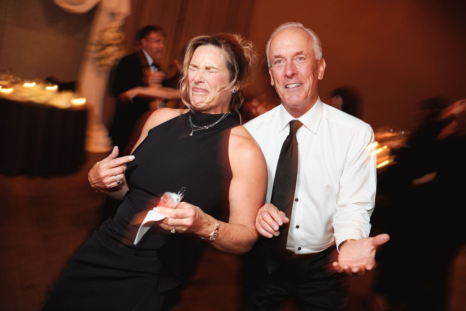 A couple in formal attire dancing together at an event, with the woman in black and man in white shirt.