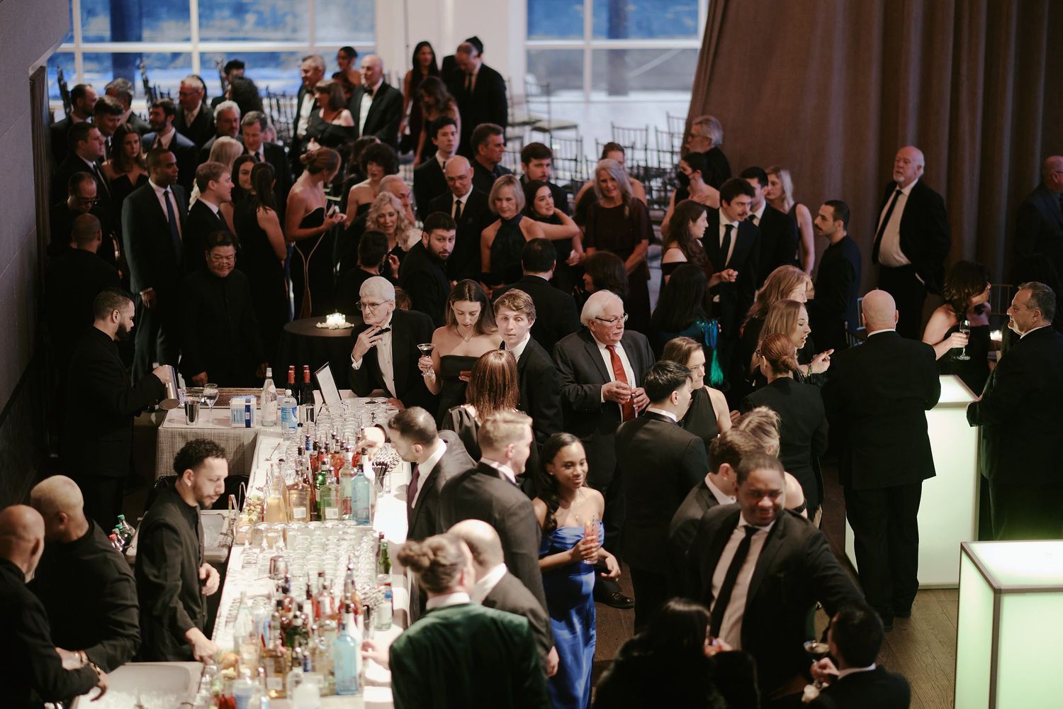 Overhead view of a crowded formal event with guests gathered around elegantly set dining tables at an indoor venue.