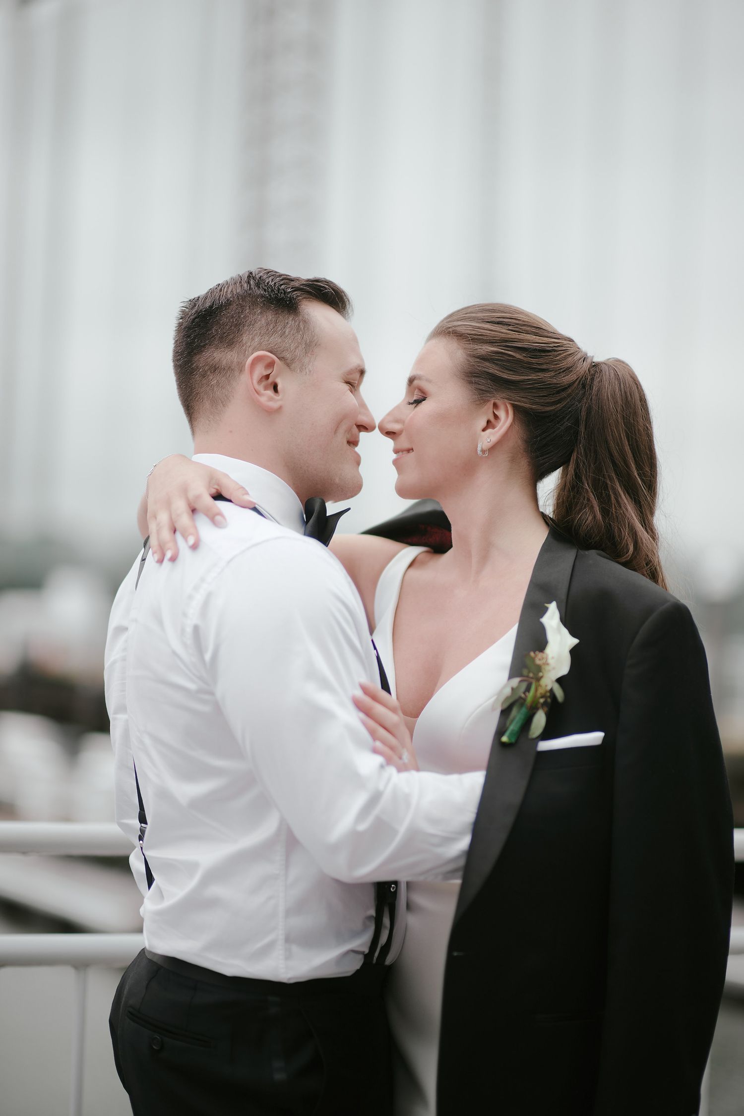 A romantic couple in formal attire sharing an intimate moment against a light backdrop.