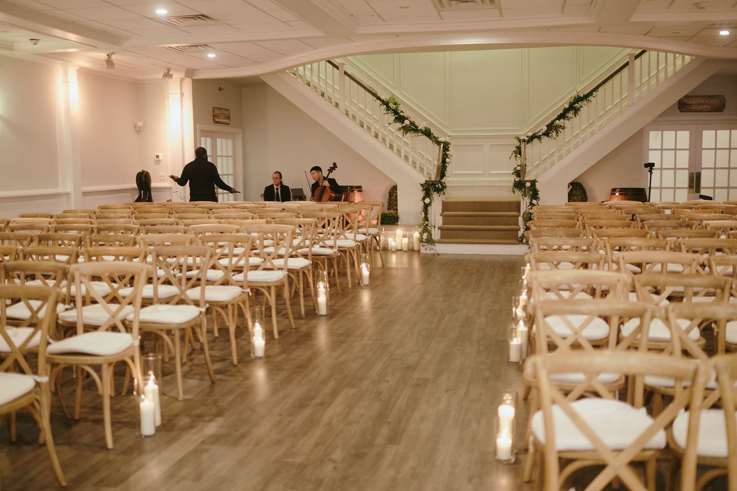 A spacious wedding ceremony venue with wooden chairs lined up facing a grand staircase decorated with elegant garlands.