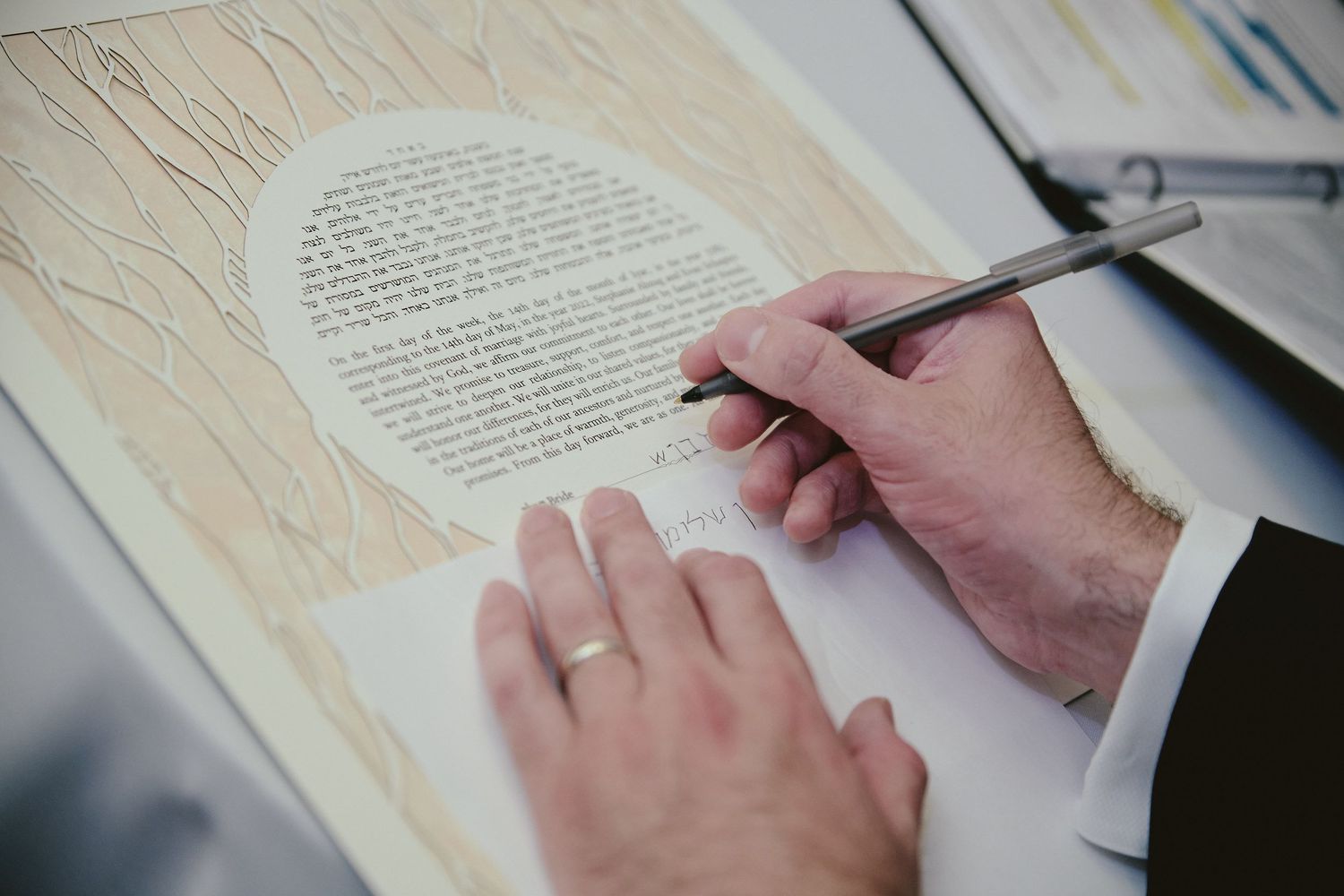Hands hold a pen while writing on a textured paper document with printed text.