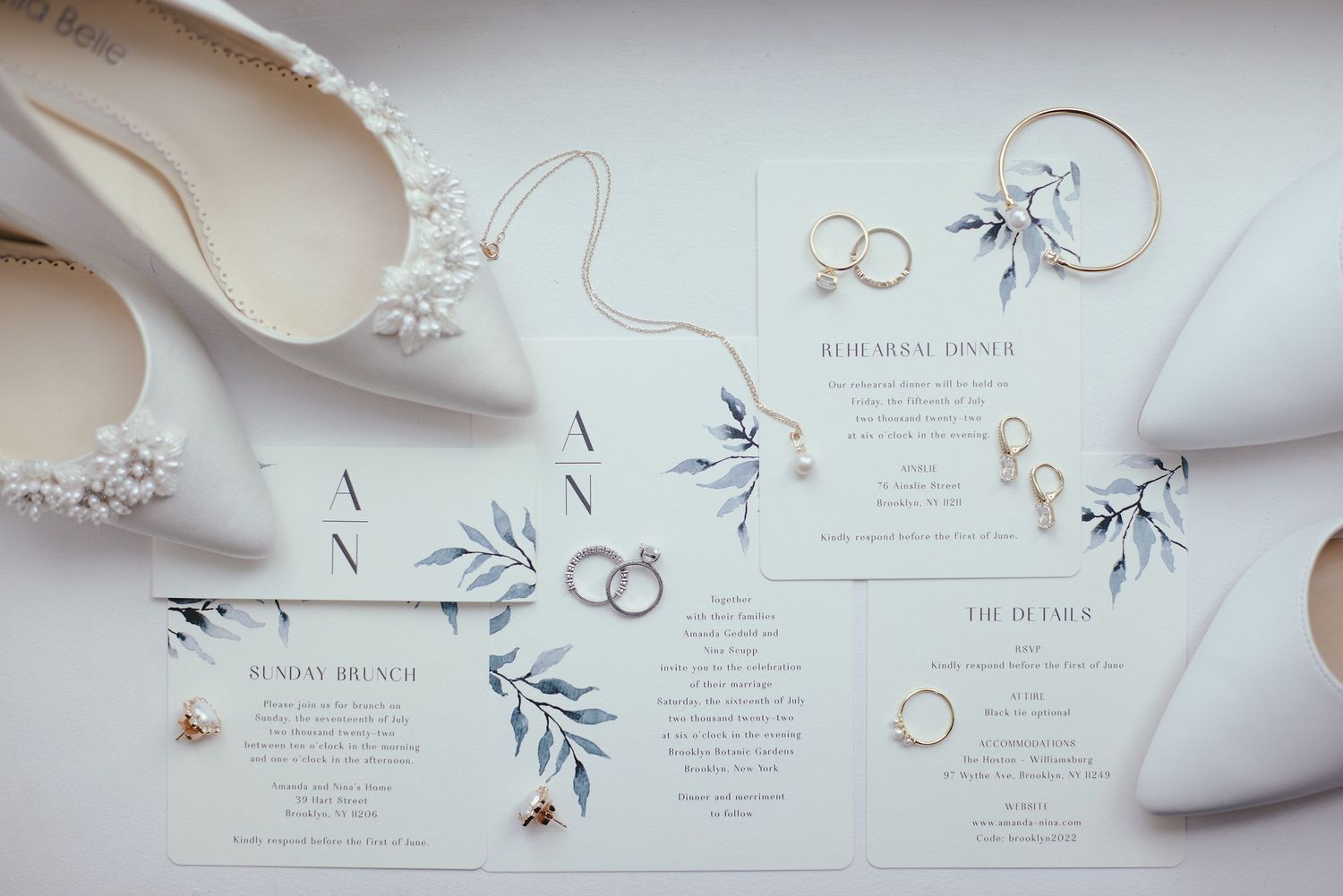 Wedding invitation suite with delicate floral designs and rings displayed alongside white bridal shoes and accessories.