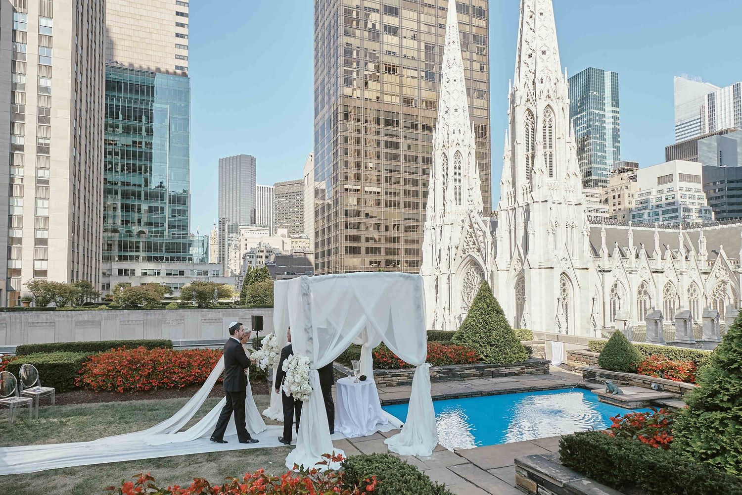 Wedding ceremony being held on a rooftop garden terrace with St. Patrick's Cathedral and Manhattan skyscrapers in background.