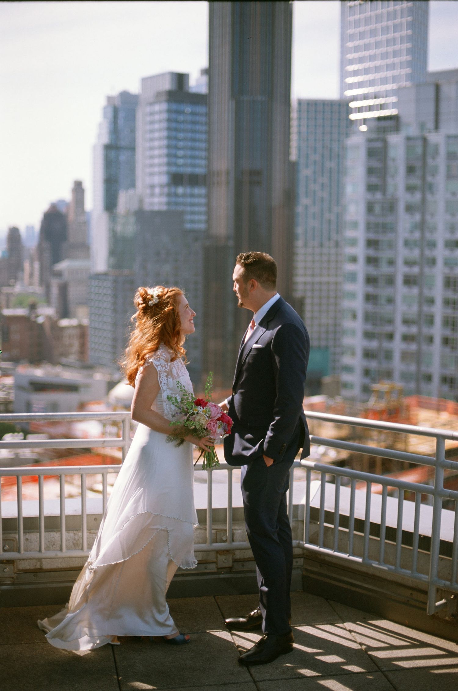 Newlywed couple shares a romantic moment on a rooftop terrace overlooking a city skyline of tall buildings.