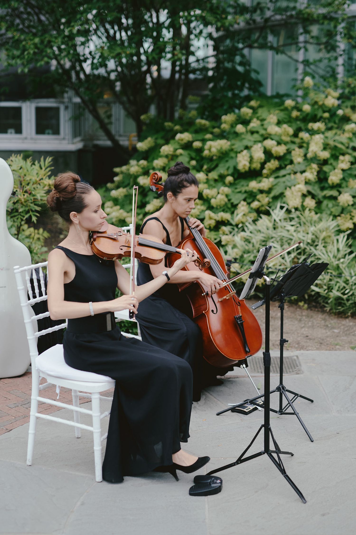 Two musicians in black dresses perform with violin and cello at an outdoor event.