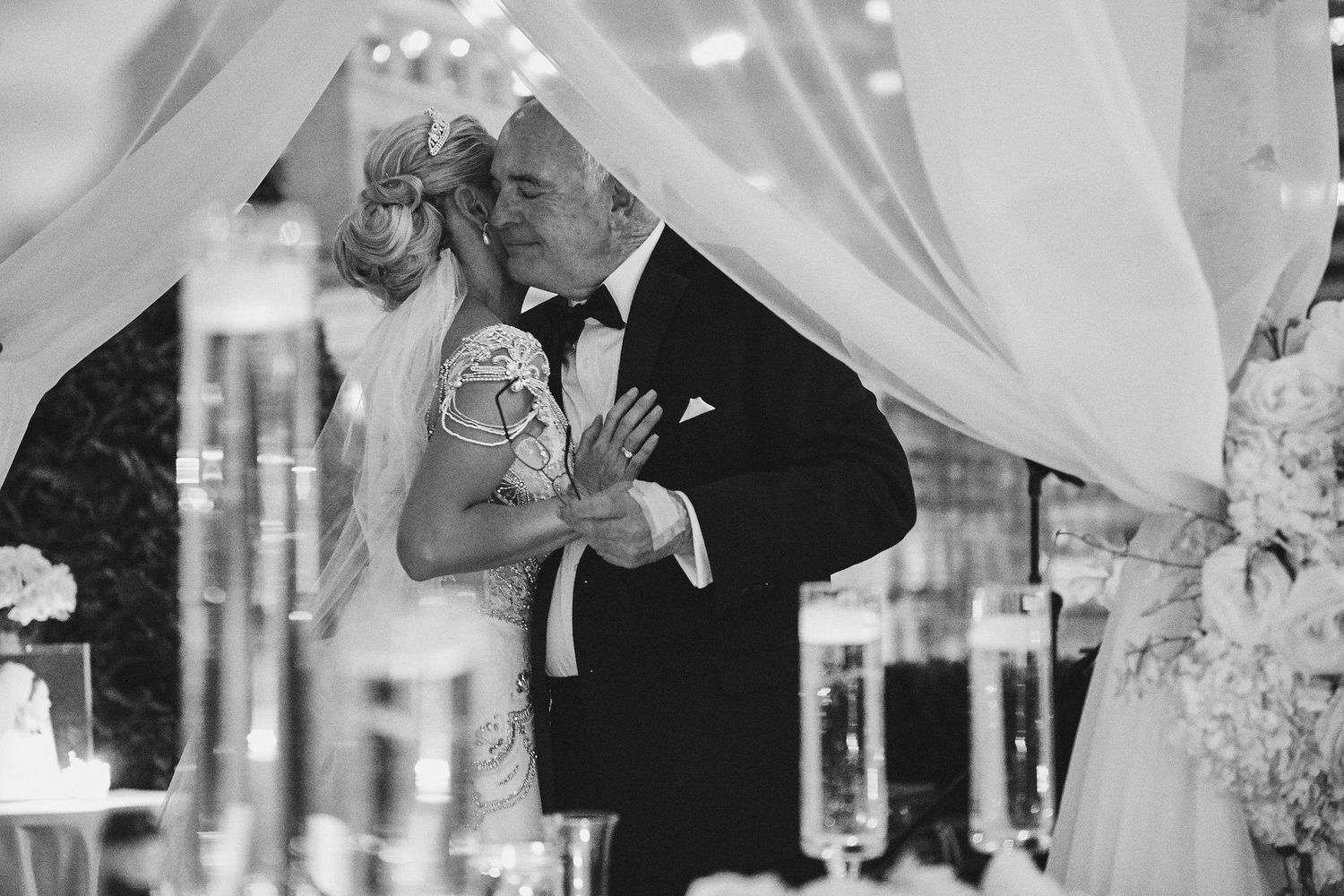 A romantic moment captured in black and white under white draping at an elegant wedding reception.
