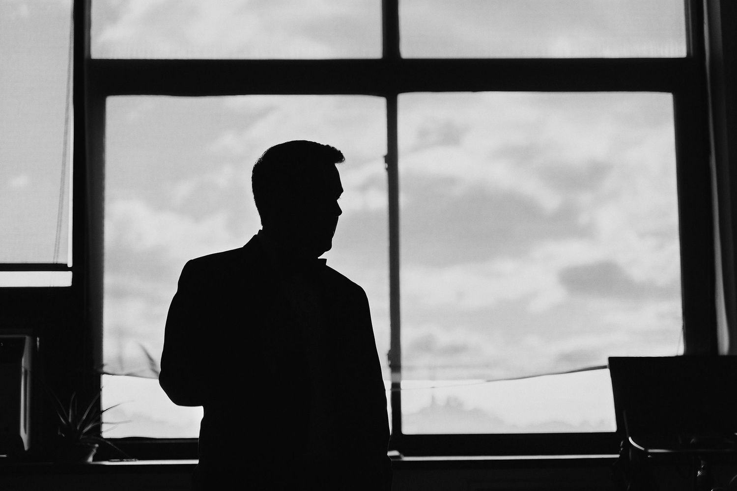 Silhouette of person looking through window at cloudy sky in black and white.