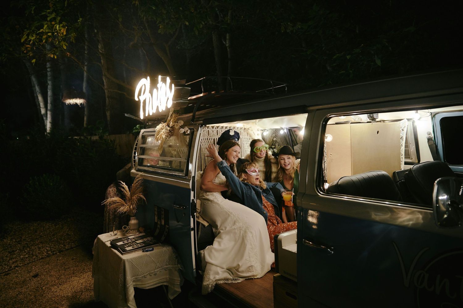 People gather at night around an illuminated vintage blue Volkswagen van while camping.