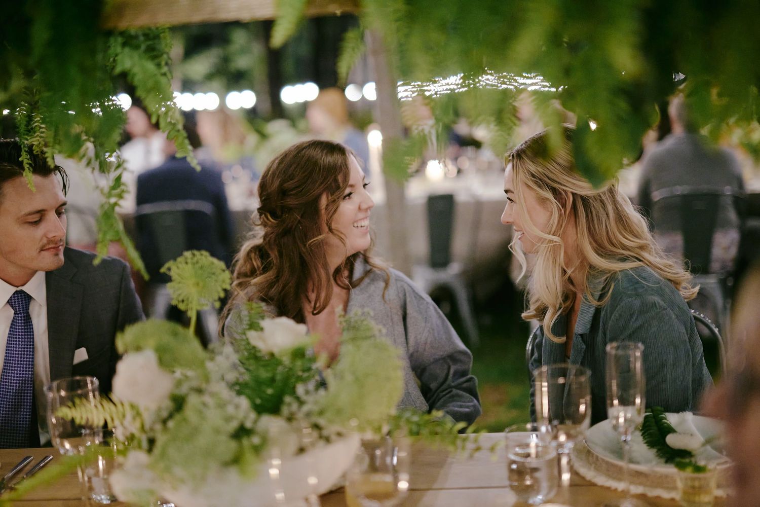 Guests enjoying conversation at an elegant outdoor dinner party with wine glasses and floral centerpieces on the table.