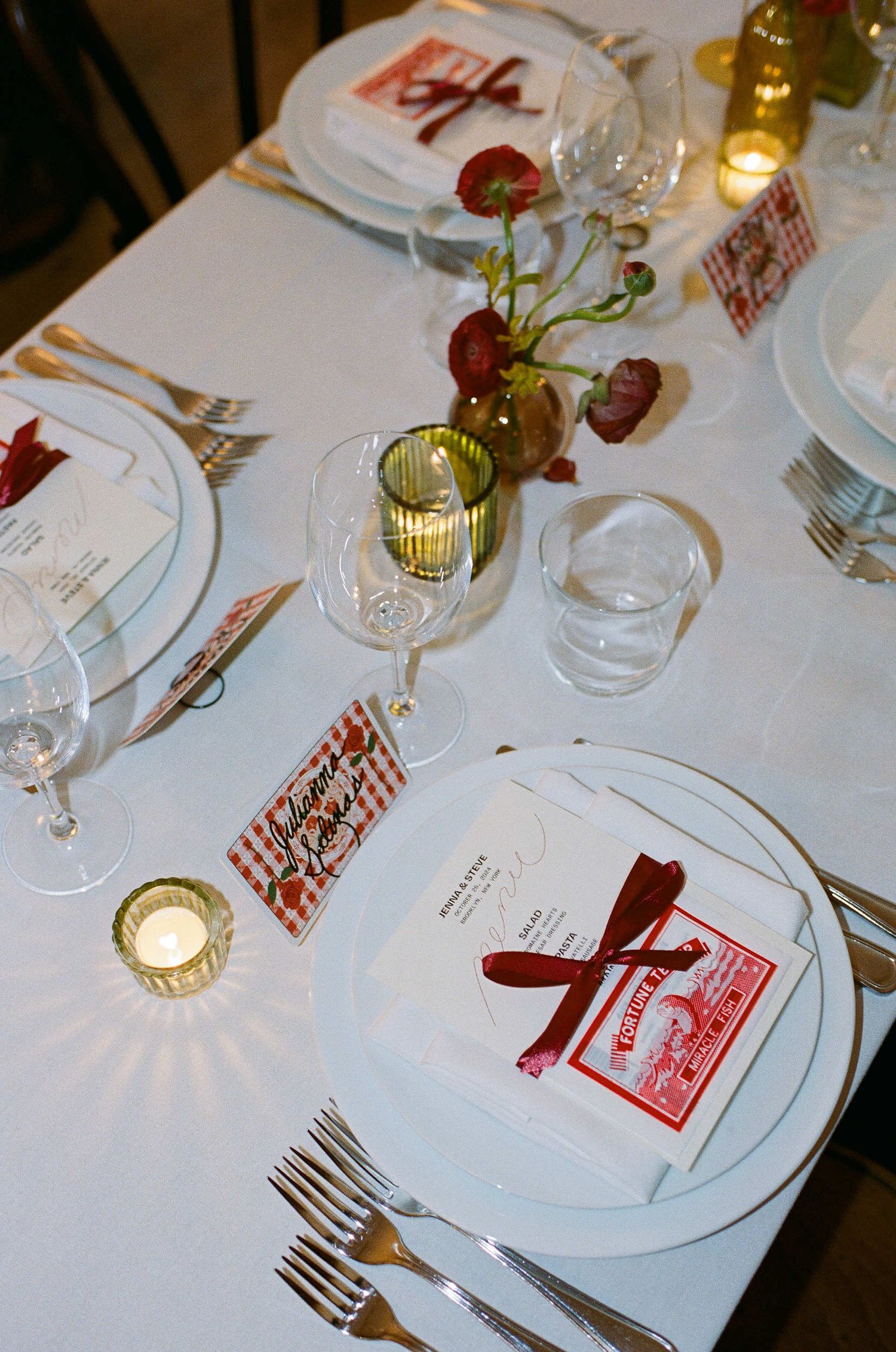 An elegant wedding table setting with white linens, red accents, wine glasses and floral centerpieces.