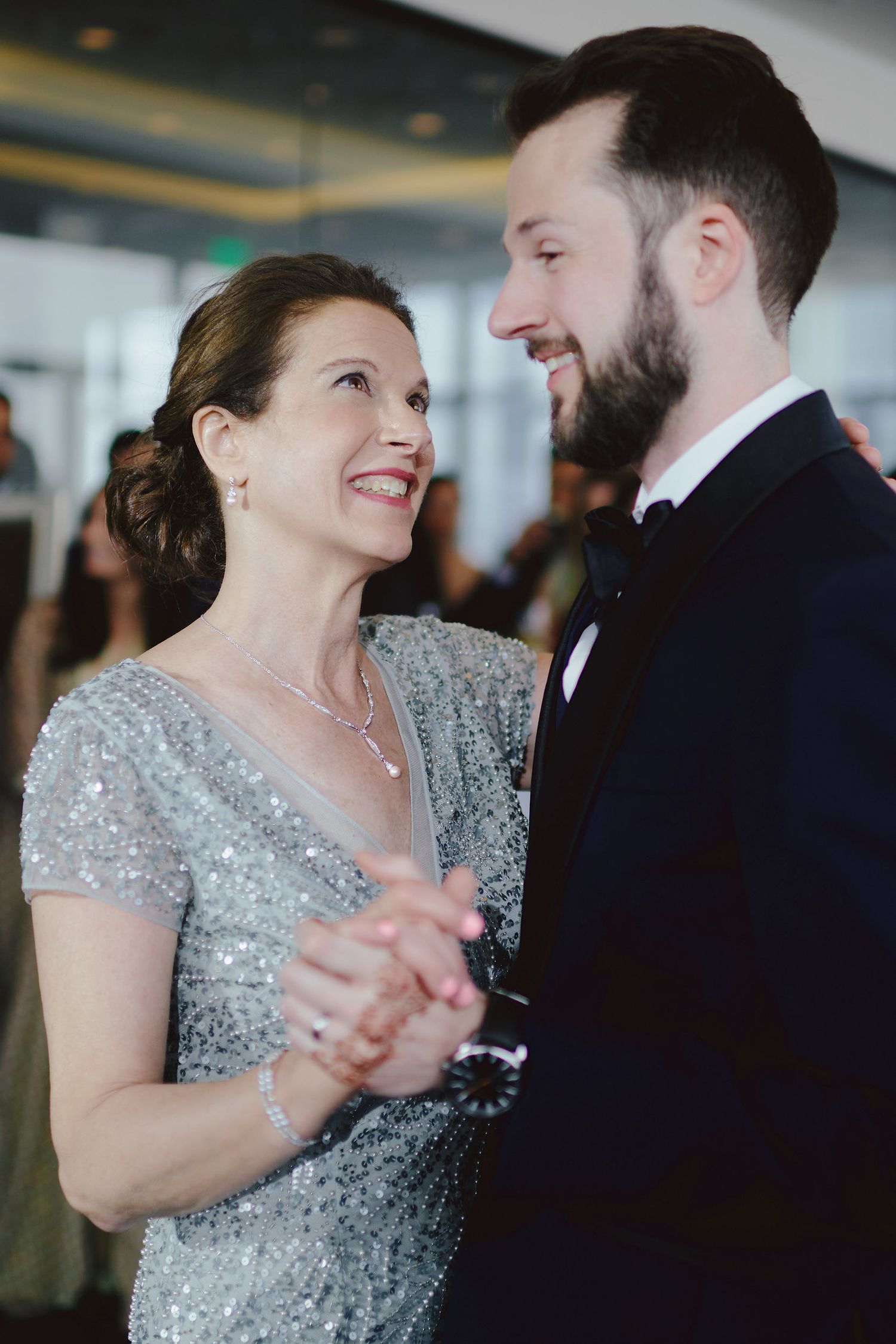 A couple shares a tender moment while dancing together, with the woman wearing a sparkly silver dress at a formal event.