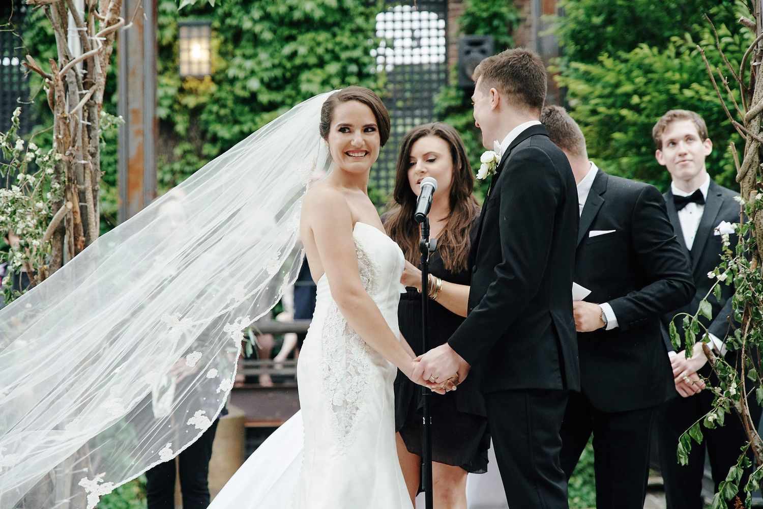 A wedding ceremony takes place in a lush garden setting with lanterns and decorative elements.