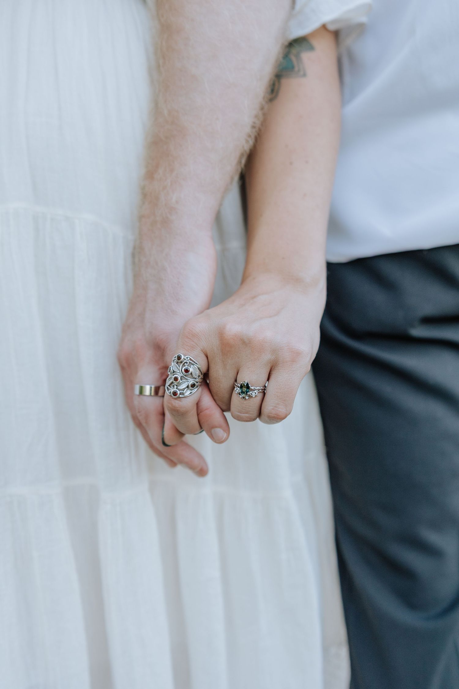 Close-up of hands wearing vintage-style engagement and wedding rings against white fabric.