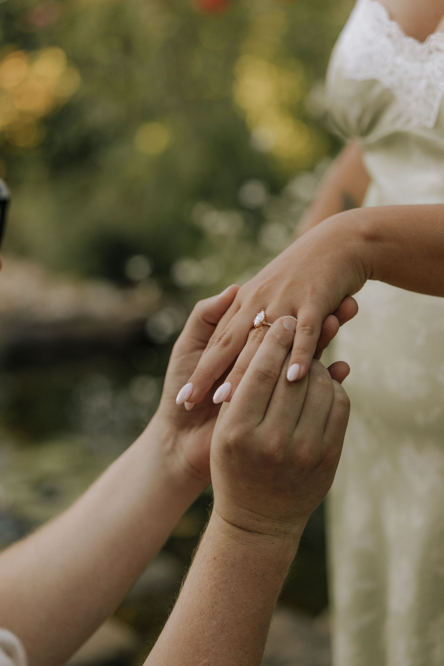 Close-up of a groom placing a diamond engagement ring on the bride's finger during a wedding ceremony outdoors.