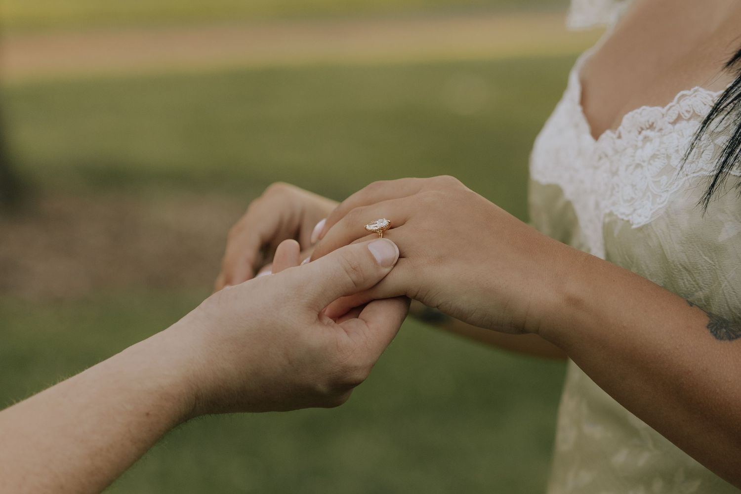 Close-up of a bride placing a wedding ring on her partner's finger during an outdoor ceremony.