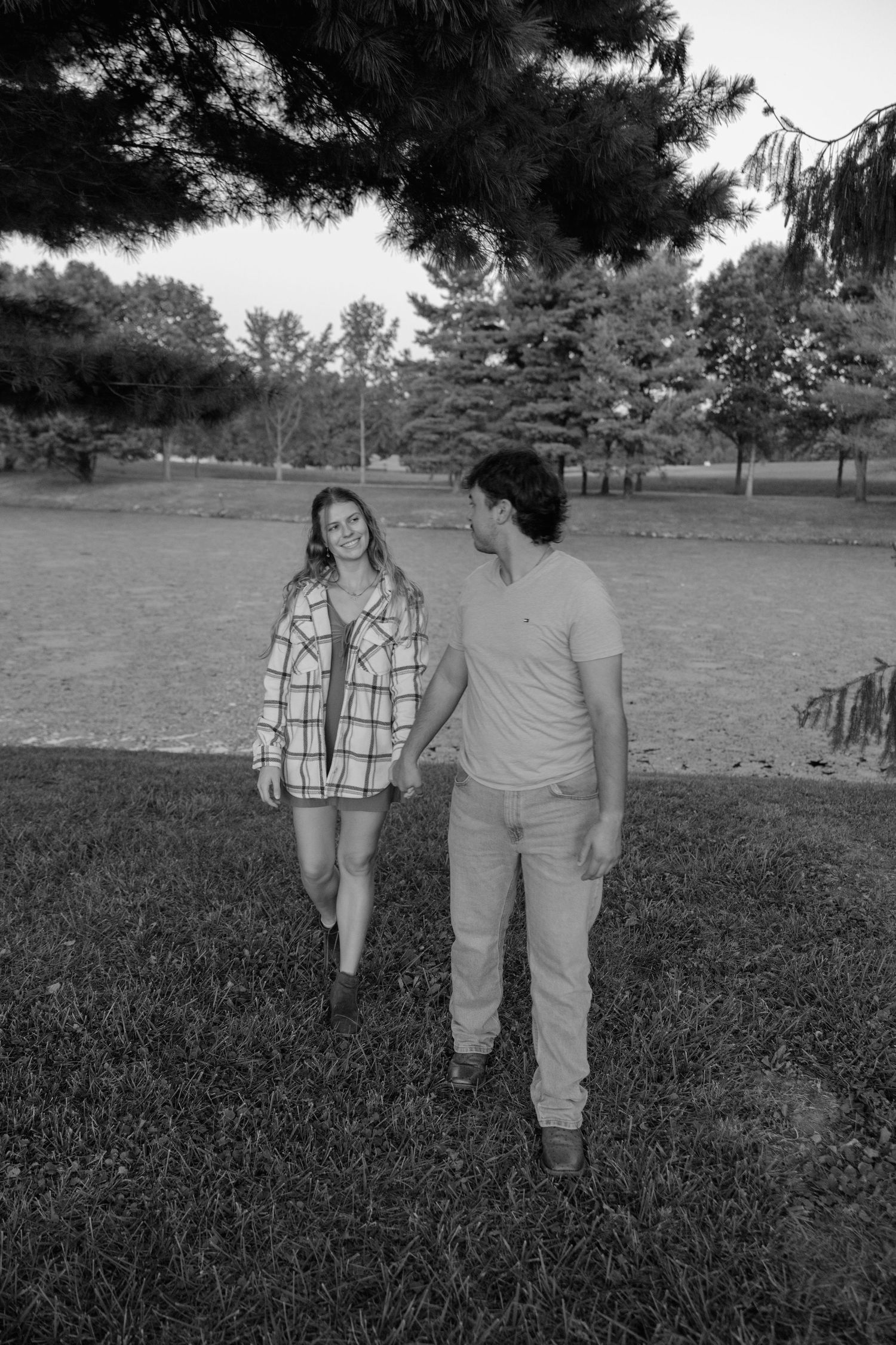 A couple walks together on a grassy lawn with trees in the background in this black and white photograph.