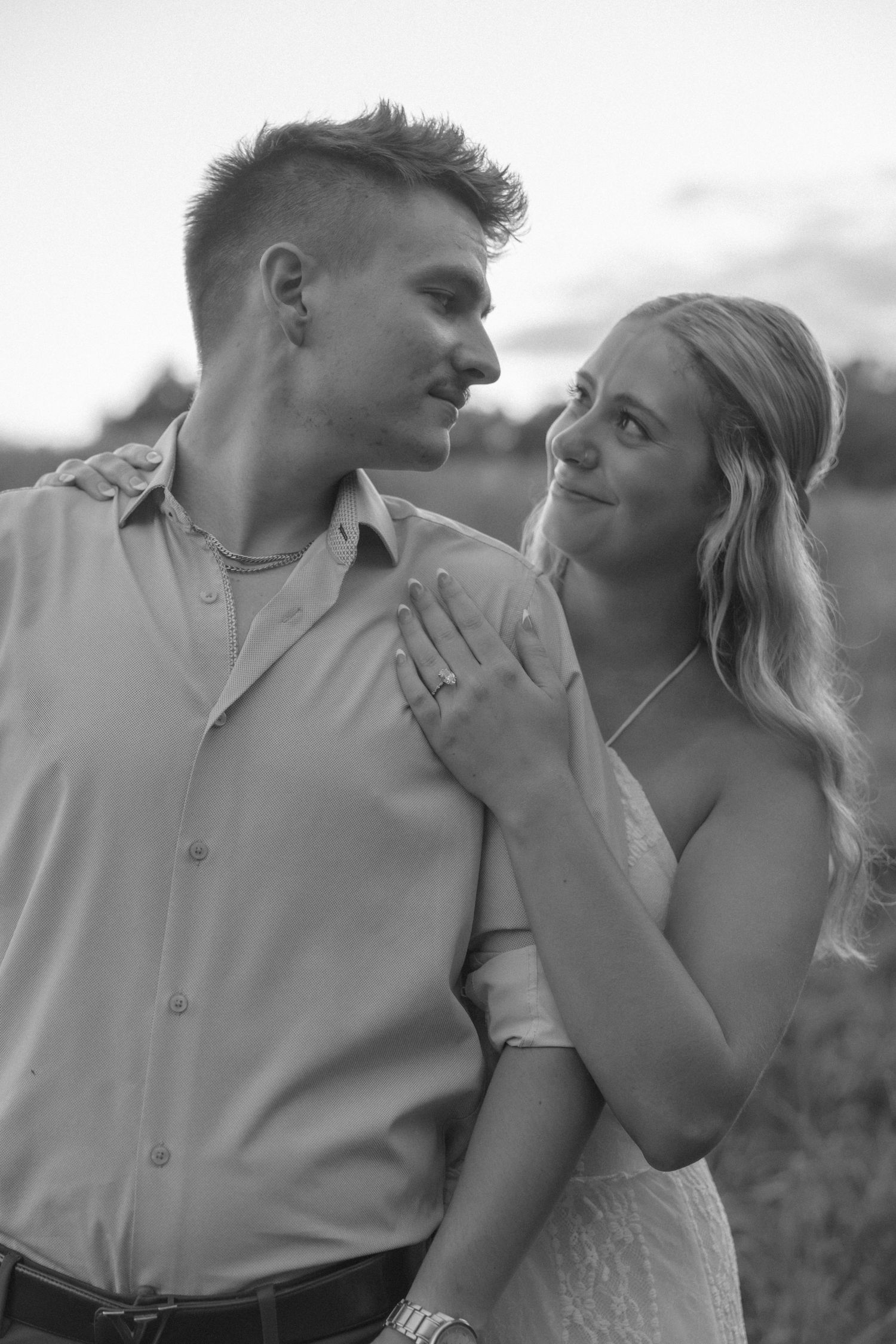 Black and white portrait of smiling bride and groom gazing at each other during outdoor shoot.