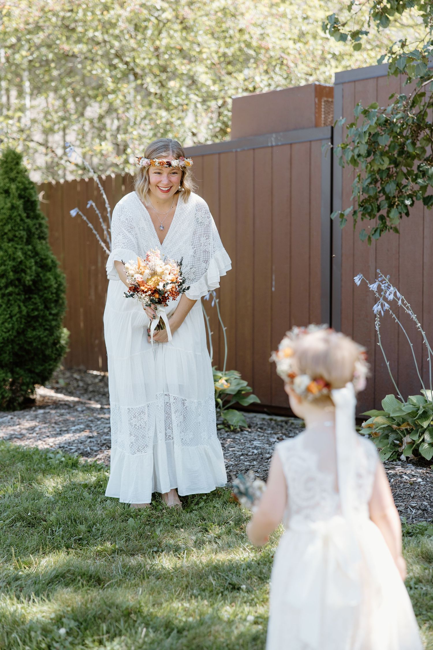 ethereal wedding photo showing a bride in white lace dress with brown fence backdrop.