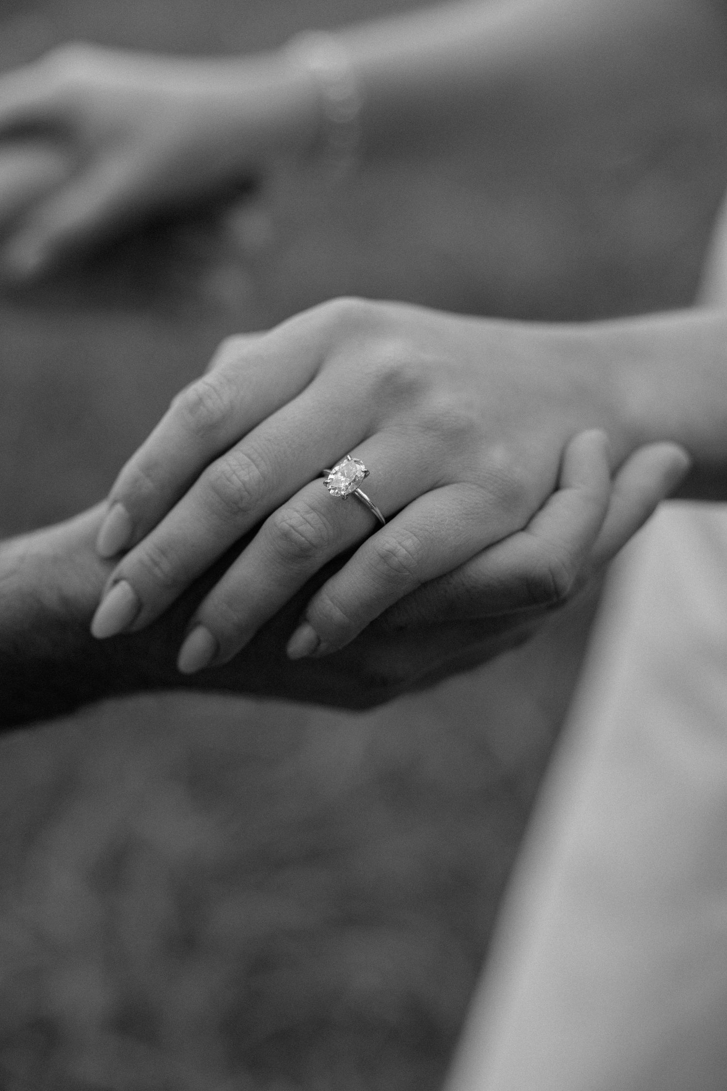 Close-up black and white photo of hands with an engagement ring showing a tender moment of connection.