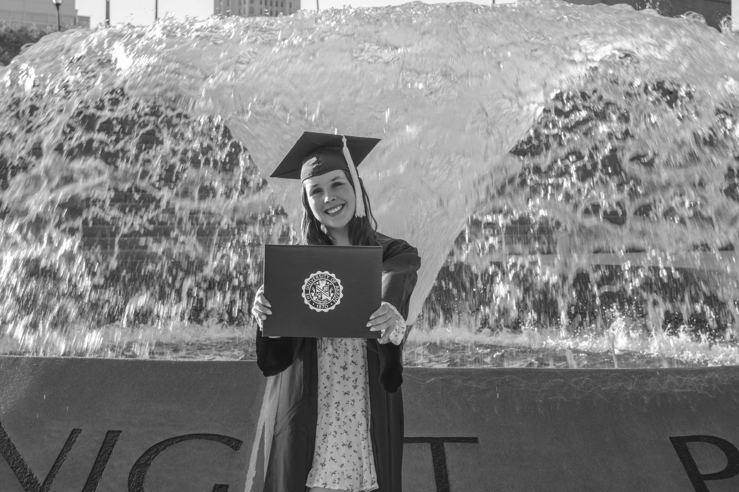 A concrete wall in a park or public setting is visible against a natural backdrop for senior photos
