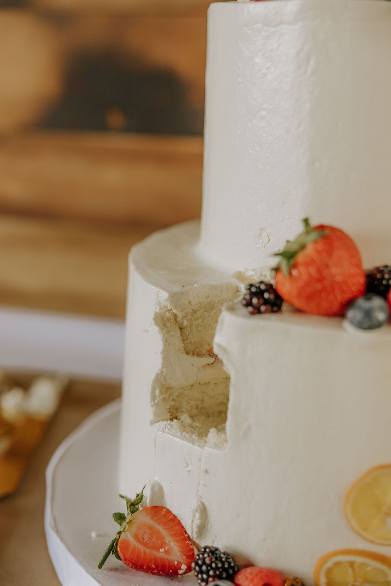 A white wedding cake decorated with fresh strawberries, blackberries and citrus slices on a white plate.