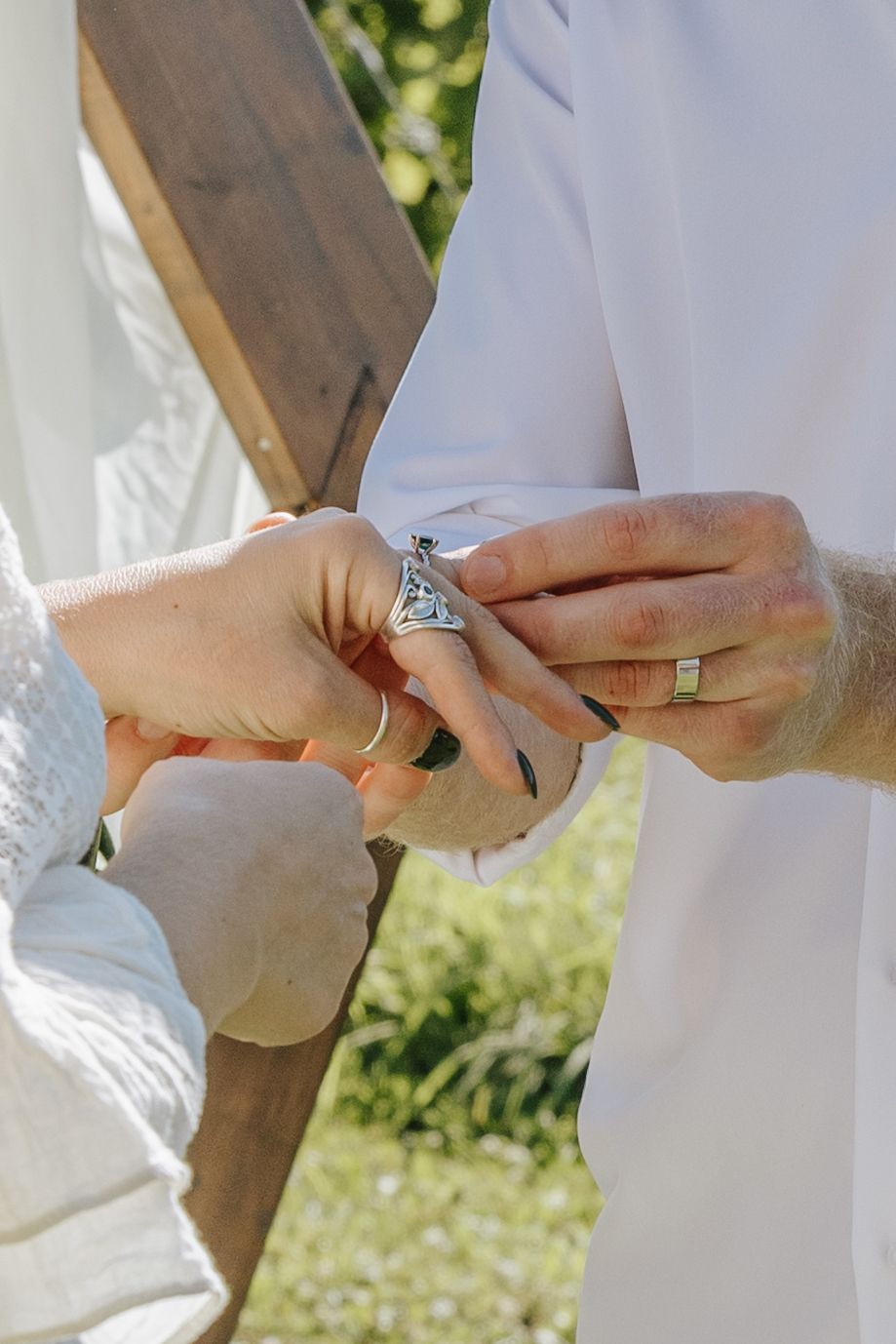 Close-up sequence of hands exchanging wedding rings during an outdoor ceremony.