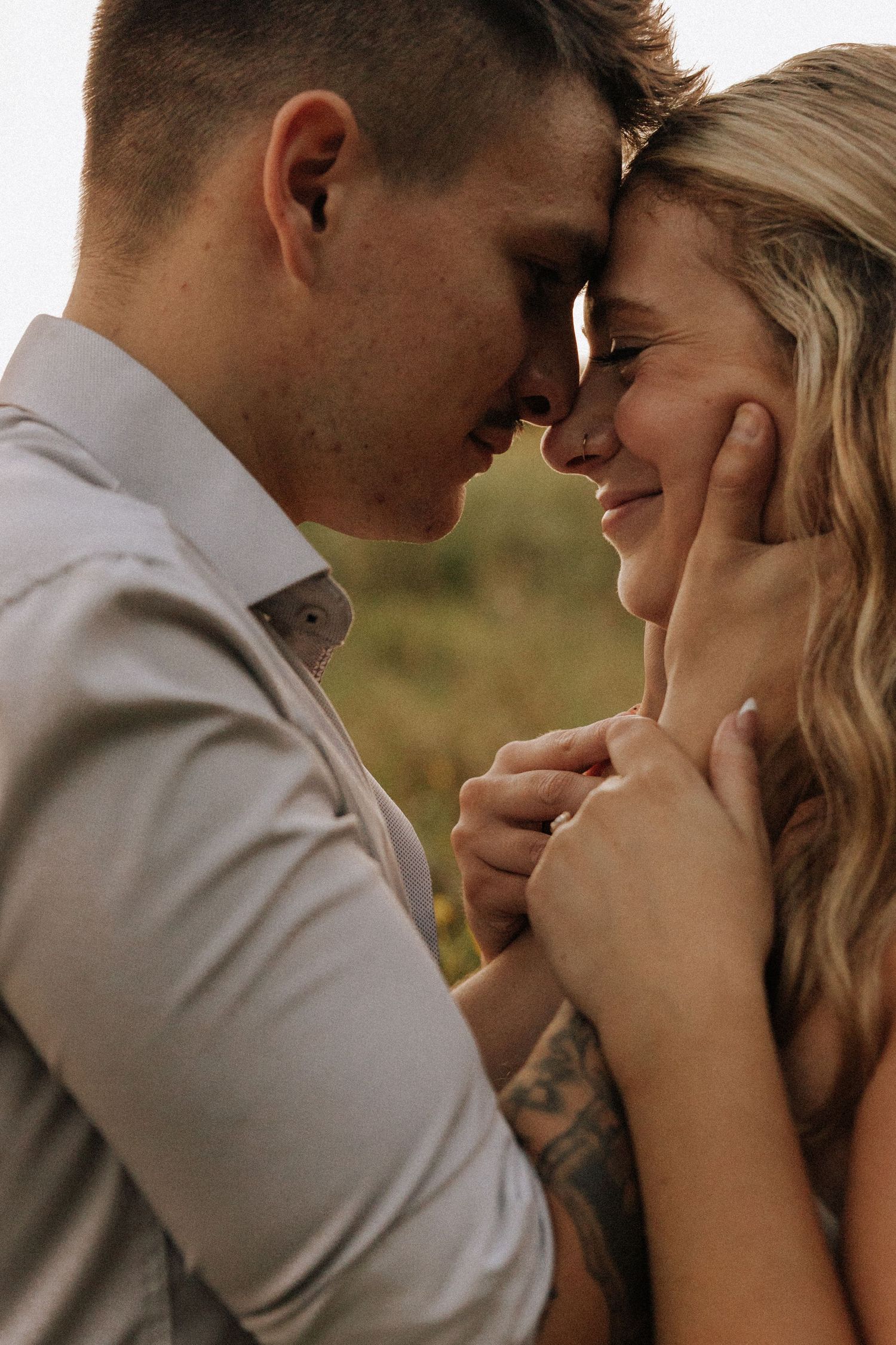 A couple tenderly touches foreheads while holding hands outdoors, sharing a romantic intimate moment together.
