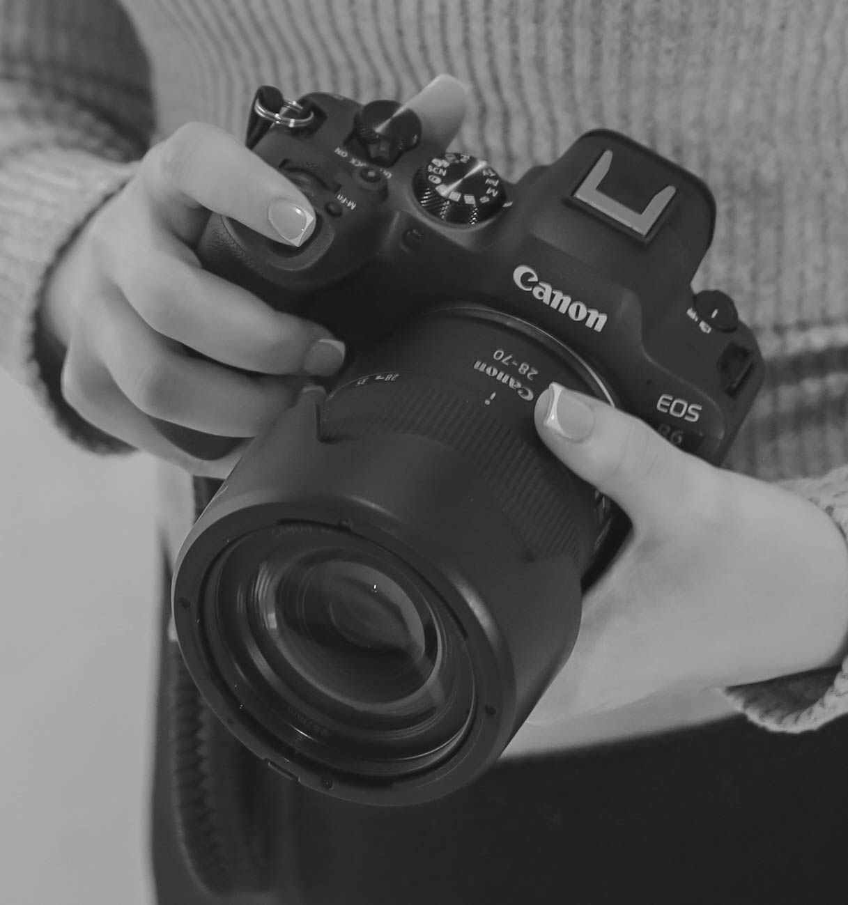 Hands holding a black Canon EOS camera with mounted lens in a black and white photo.