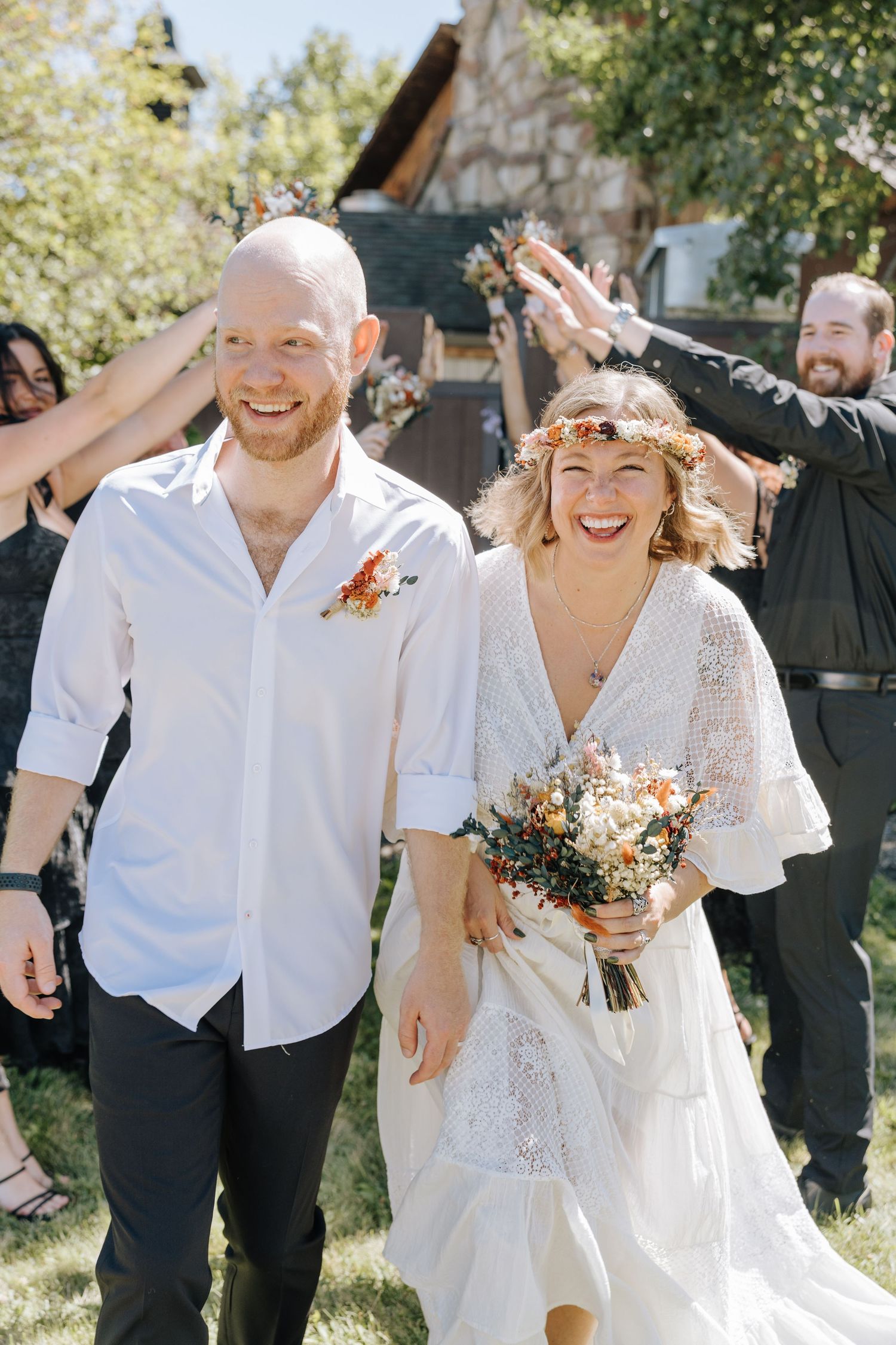 A joyful couple celebrates during their outdoor wedding ceremony while guests cheer in the background.