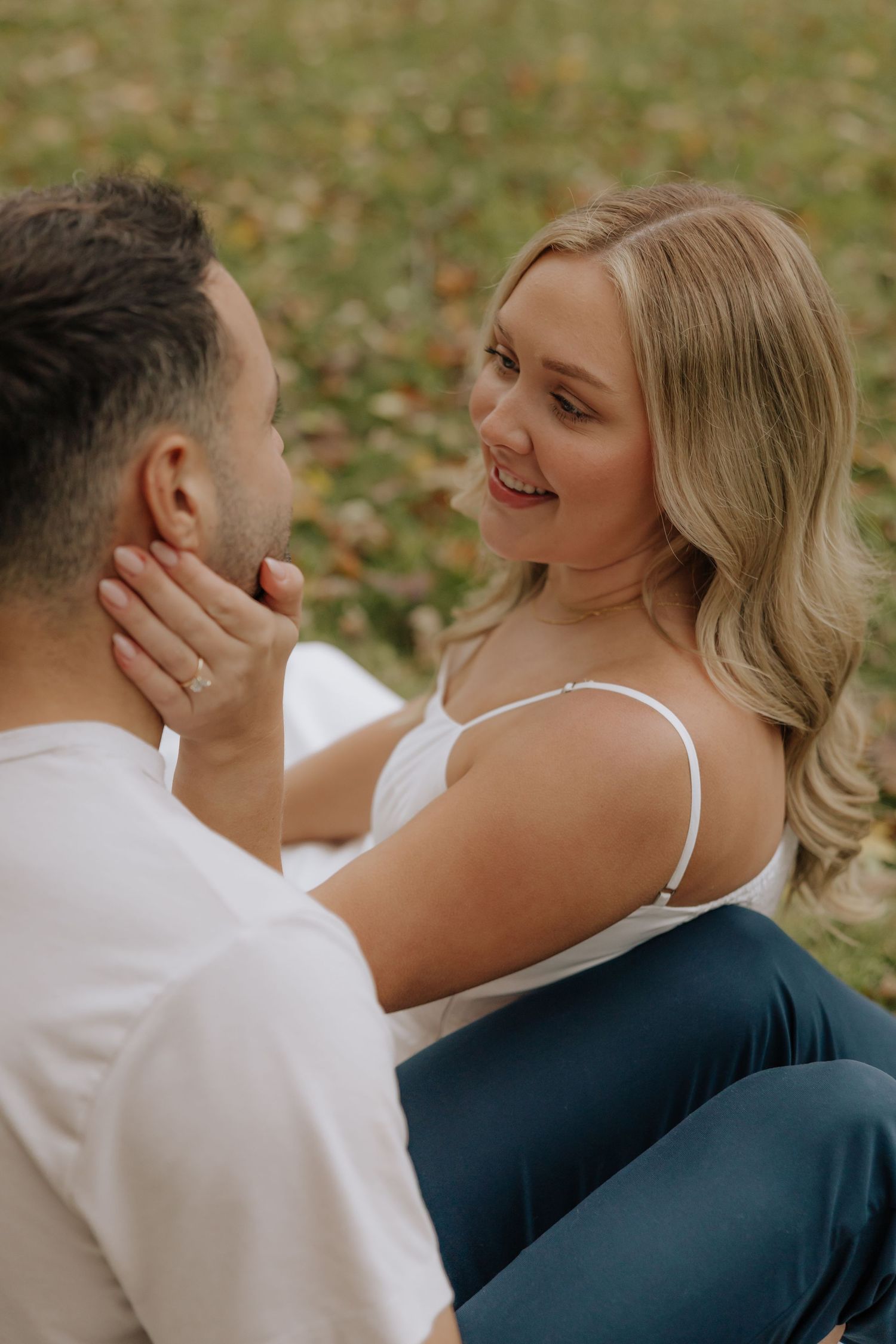 A couple shares intimate moments while sitting together on autumn leaves in a romantic outdoor photoshoot.